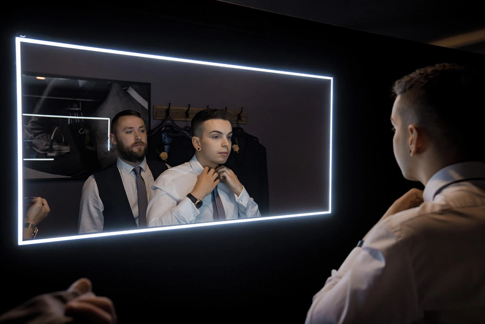 groomsmen adjust tie in mirror in den at colshaw hall wedding venue