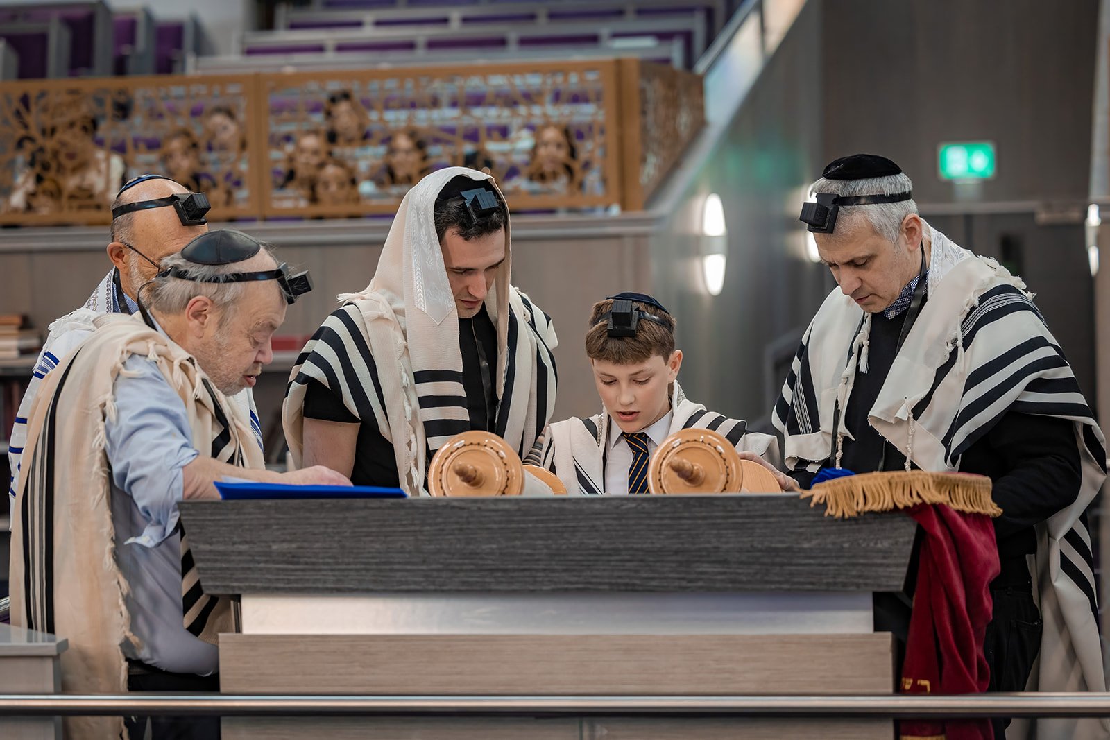barmitzvah boy on bimah reading from torah in synagogue in Manchester with family