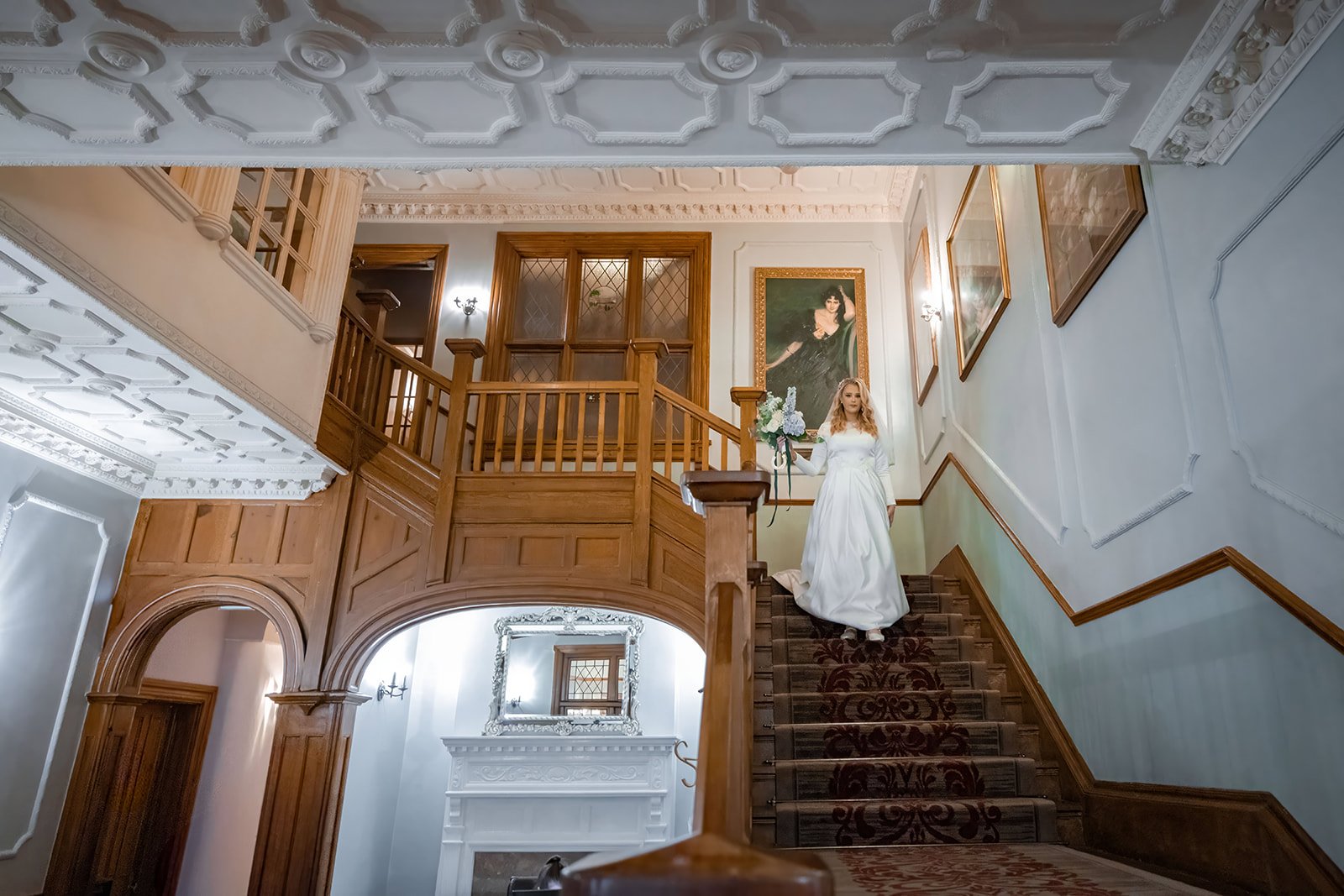 Bride descending the staircase at Nunsmere Hall in wedding dress, interior wide angle