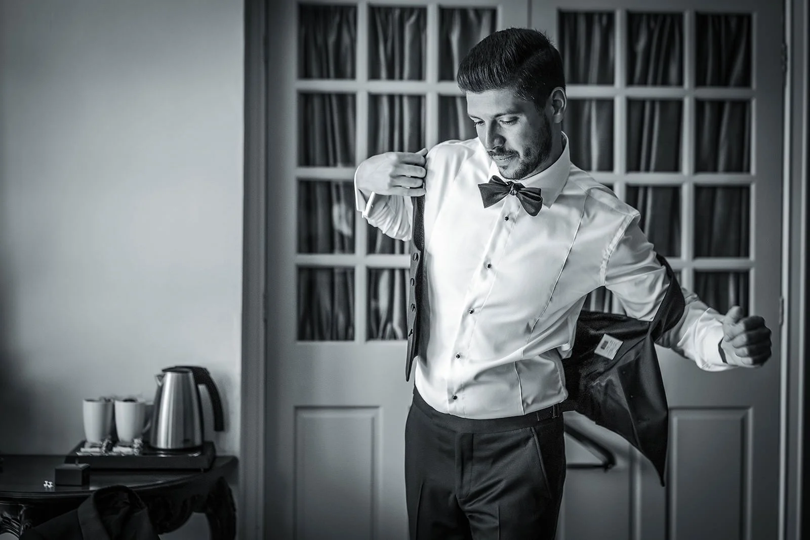 Black and white portrait of groom in bow tie by window, Nunsmere Hall wedding