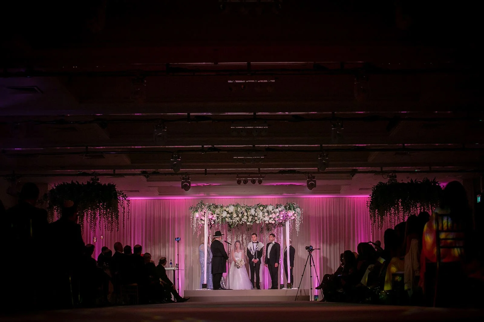 Wide ceremony shot - bride's processional under pink uplighting, floral arch, The Mere

