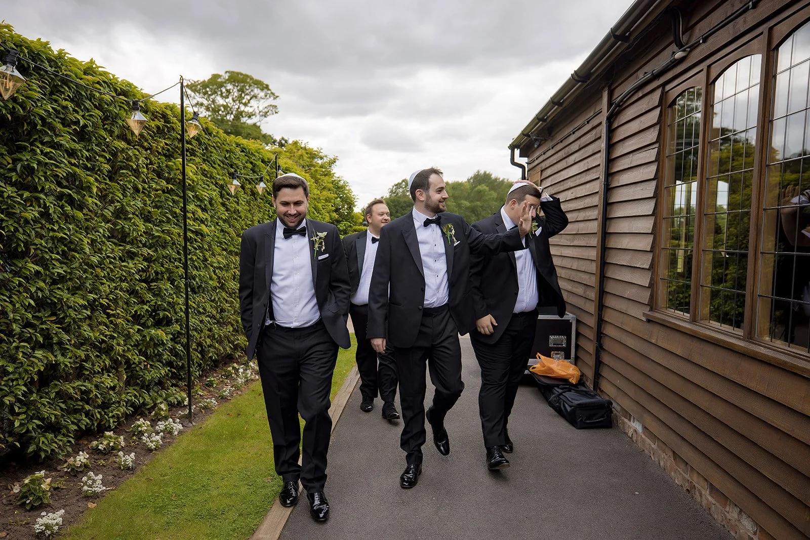 Merrydale Manor wedding groomsmen walking outdoors along hedge – documentary wedding photographer Manchester