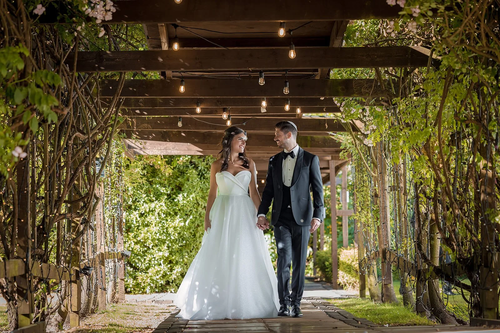 Couple walking under pergola with fairy lights at Nunsmere Hall, Cheshire
