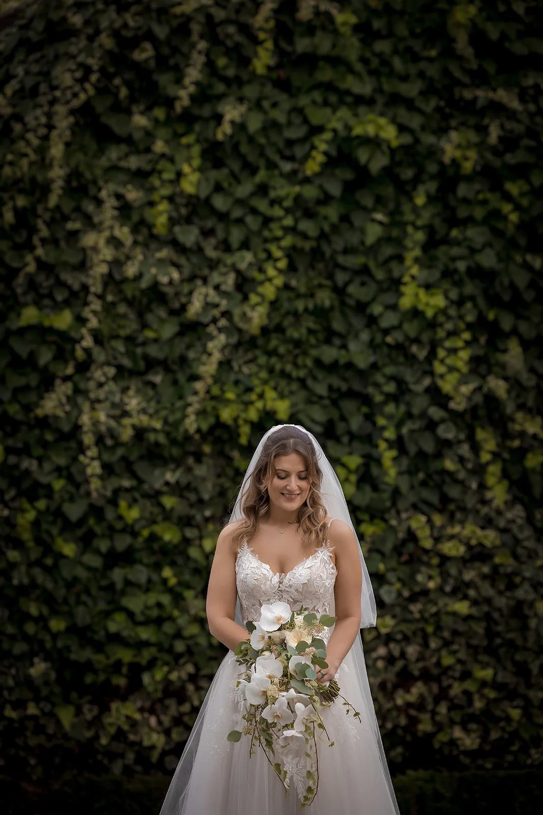 Bride with bouquet against ivy-covered wall at Fairmont Cheshire - The Mere
