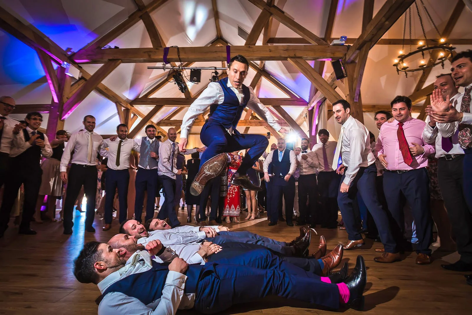Groom jumping over groomsmen during evening reception party at Sandhole Oak Barn