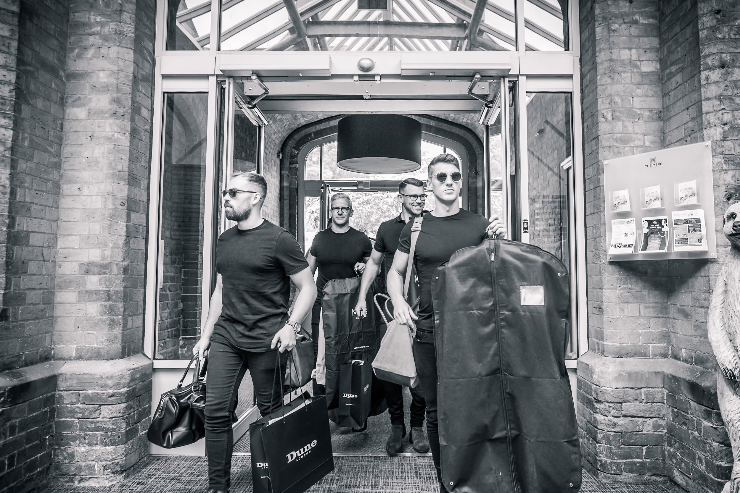Black and white - groomsmen with suit bags arriving at The Mere, Cheshire
