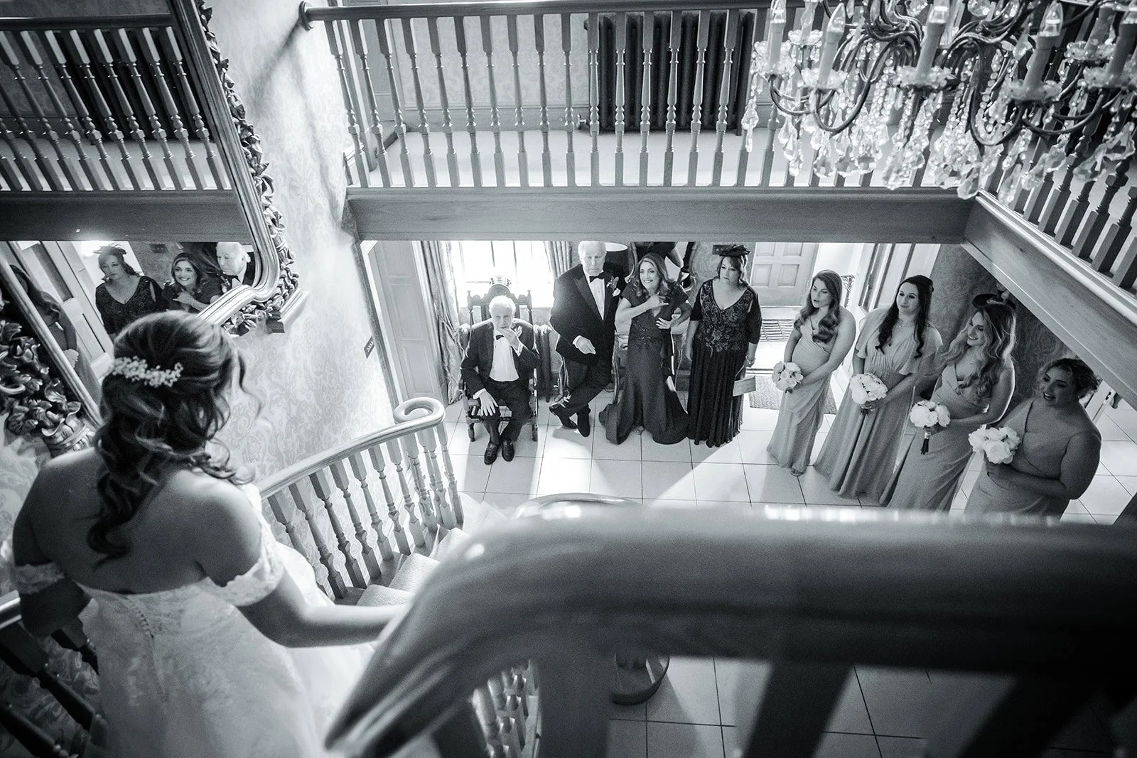 A black-and-white photo at Merrydale Manor as bride comes down staircase to see bridesmaids