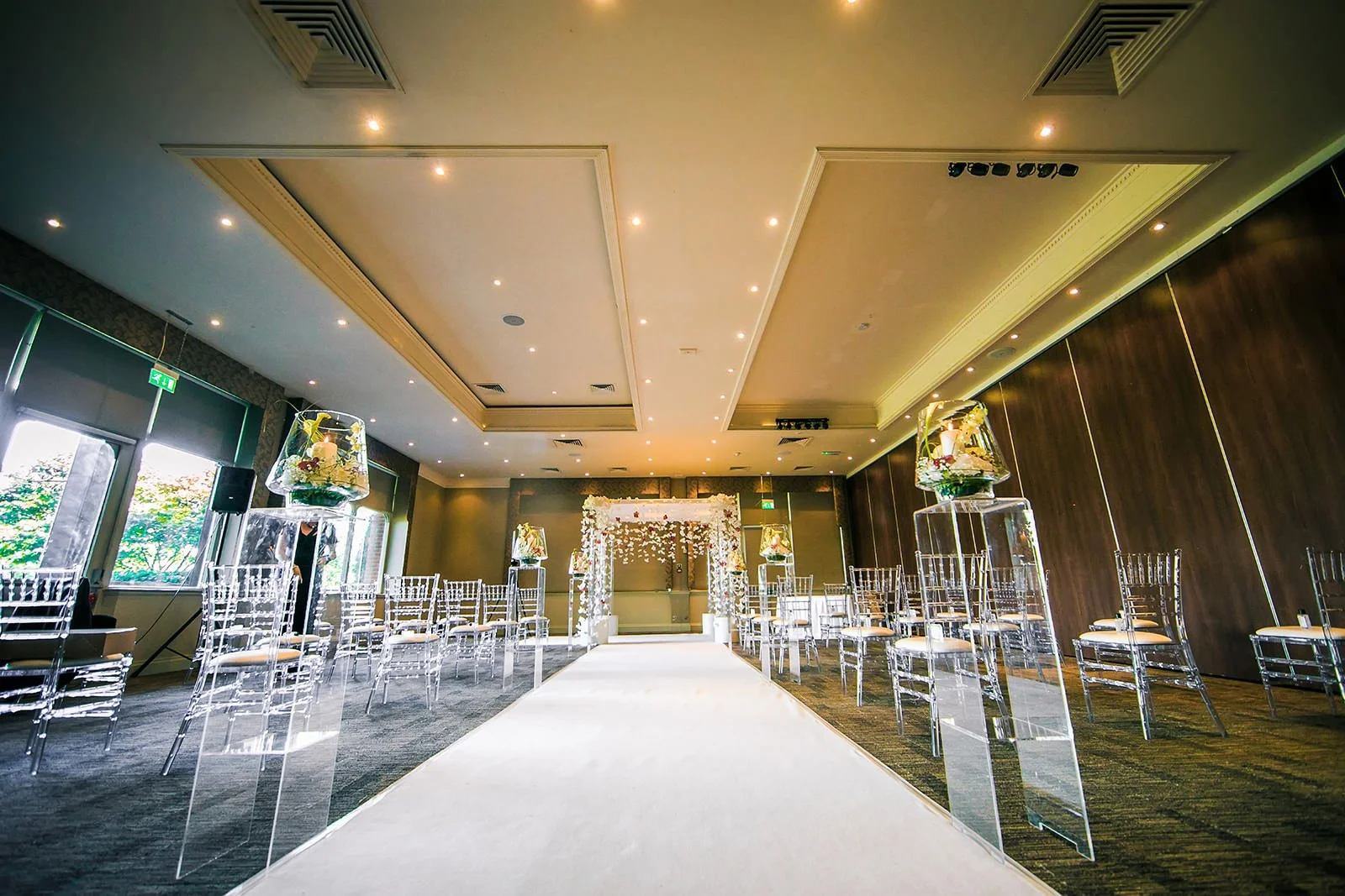 Ceremony room with ghost chairs, white aisle and tall floral columns, The Mere Knutsford
