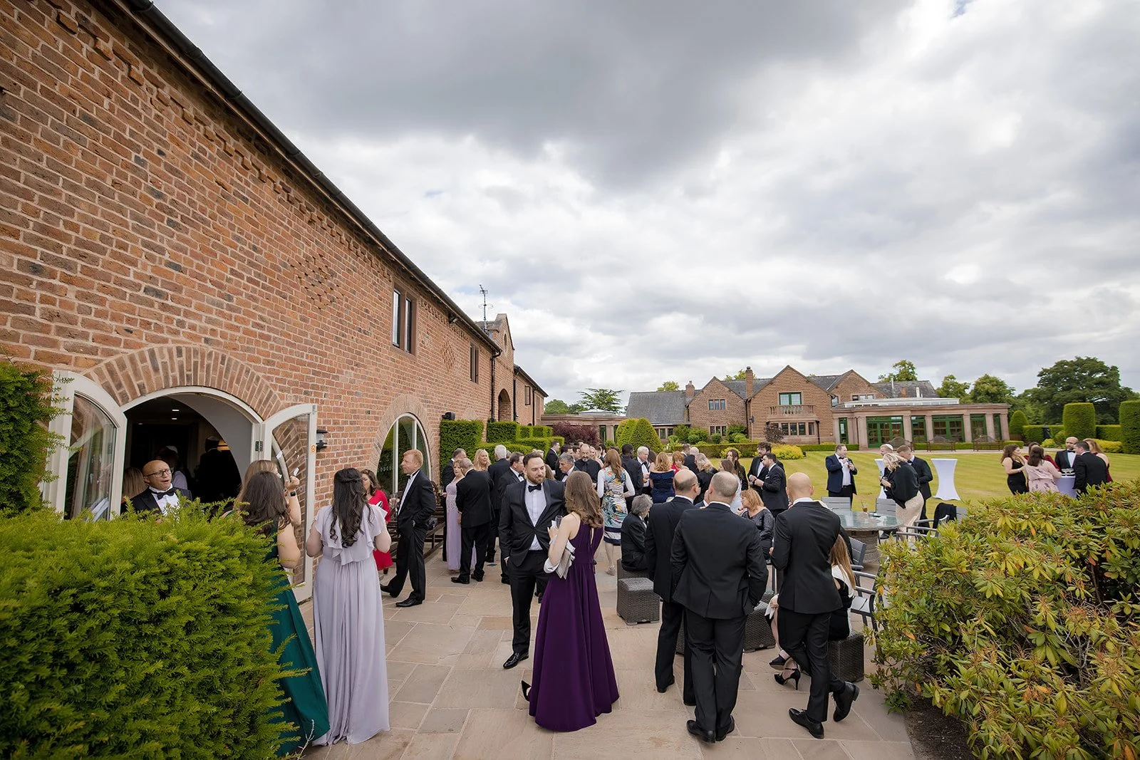 Guests dressed in formal attire at Merrydale Manor gather outside on a manicured lawn for drinks reception cocktail hour