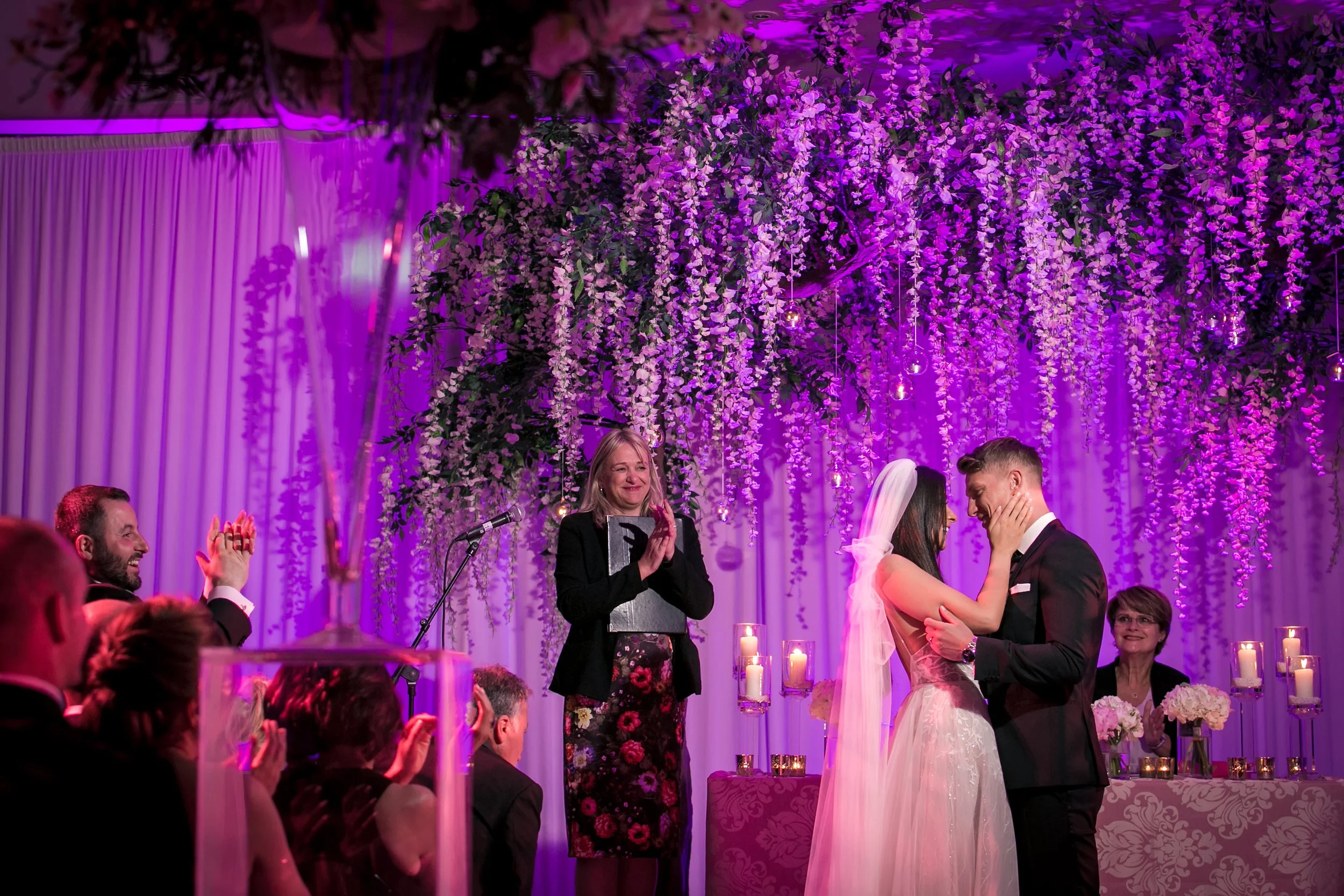 Bride and groom under wisteria-draped chuppah, purple lighting, The Mere
