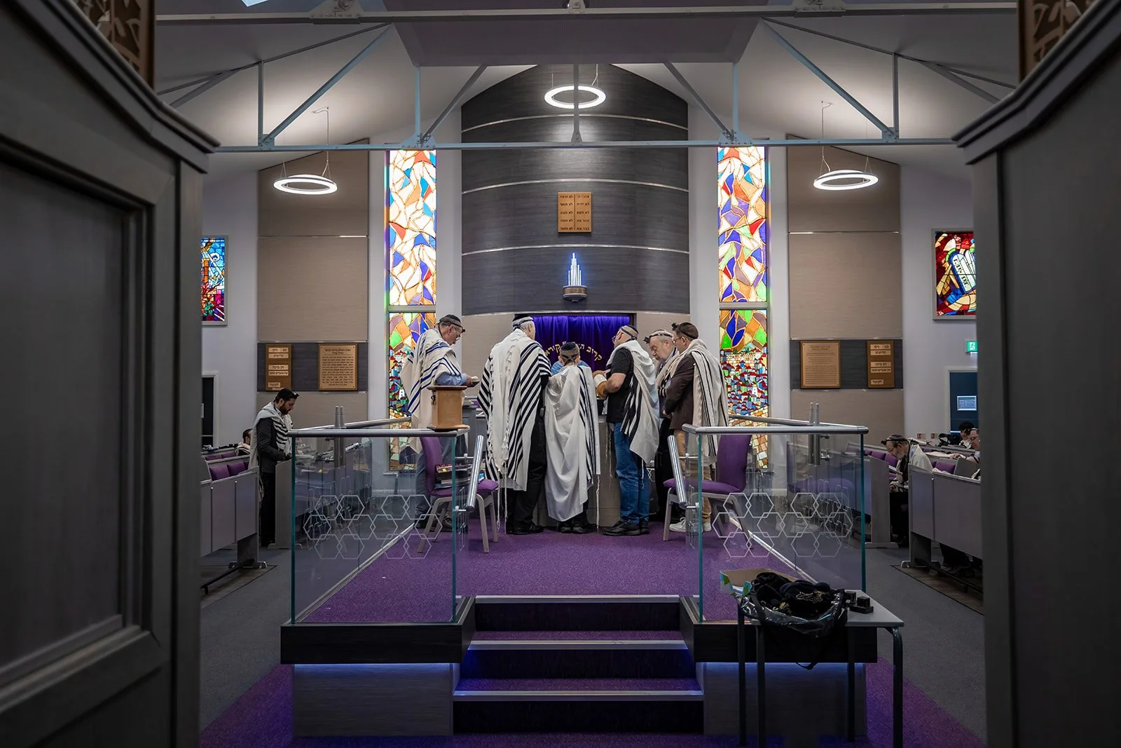 wide angle from back of synagogue of barmitzvah boy reading from torah surrounded by family in Manchester