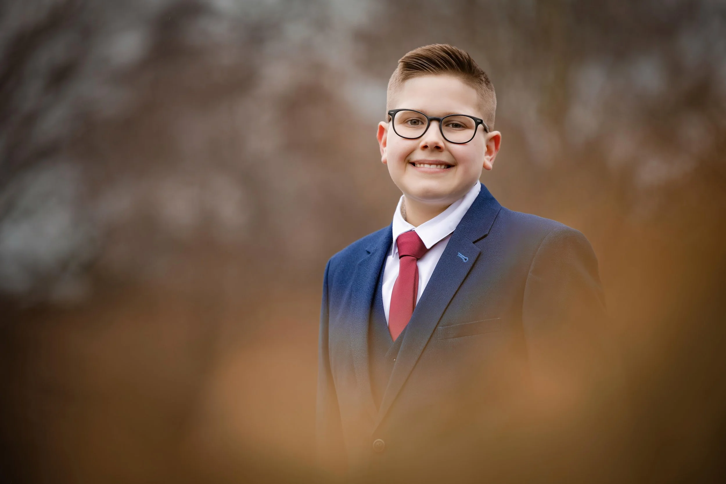 barmitzvah boy portrait in park framed by blurred leaves