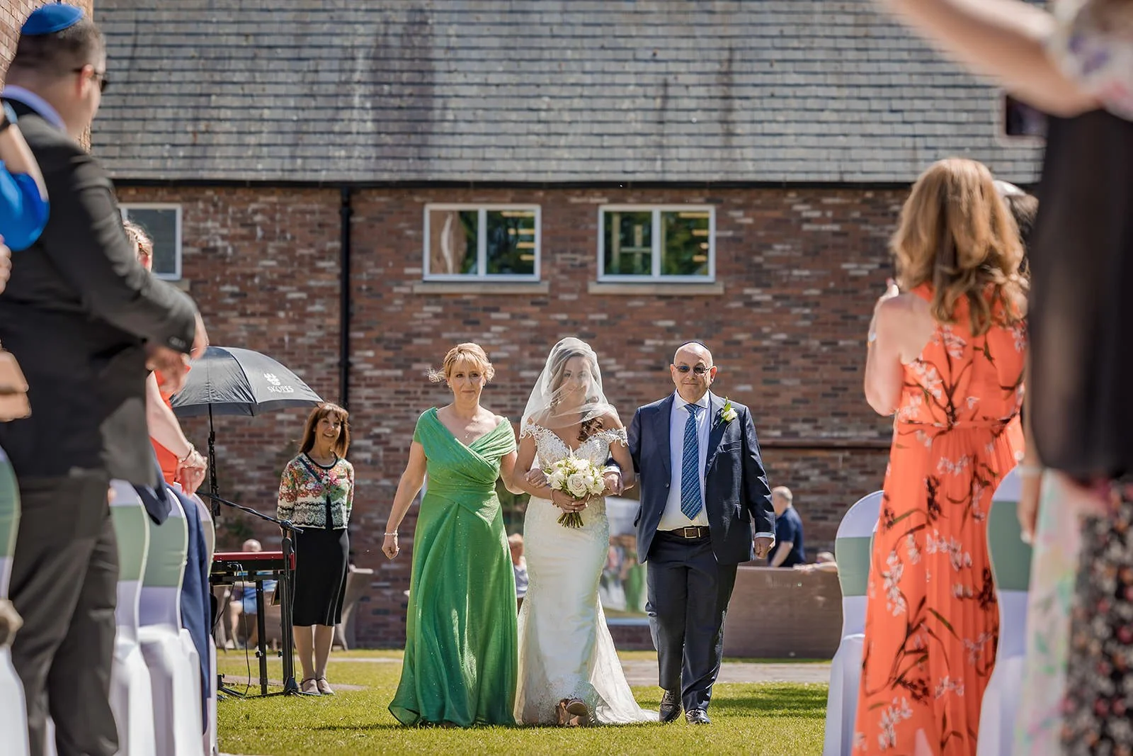 bride and parents walk down aisle at start of outdoor wedding ceremony at worsley marriott hotel