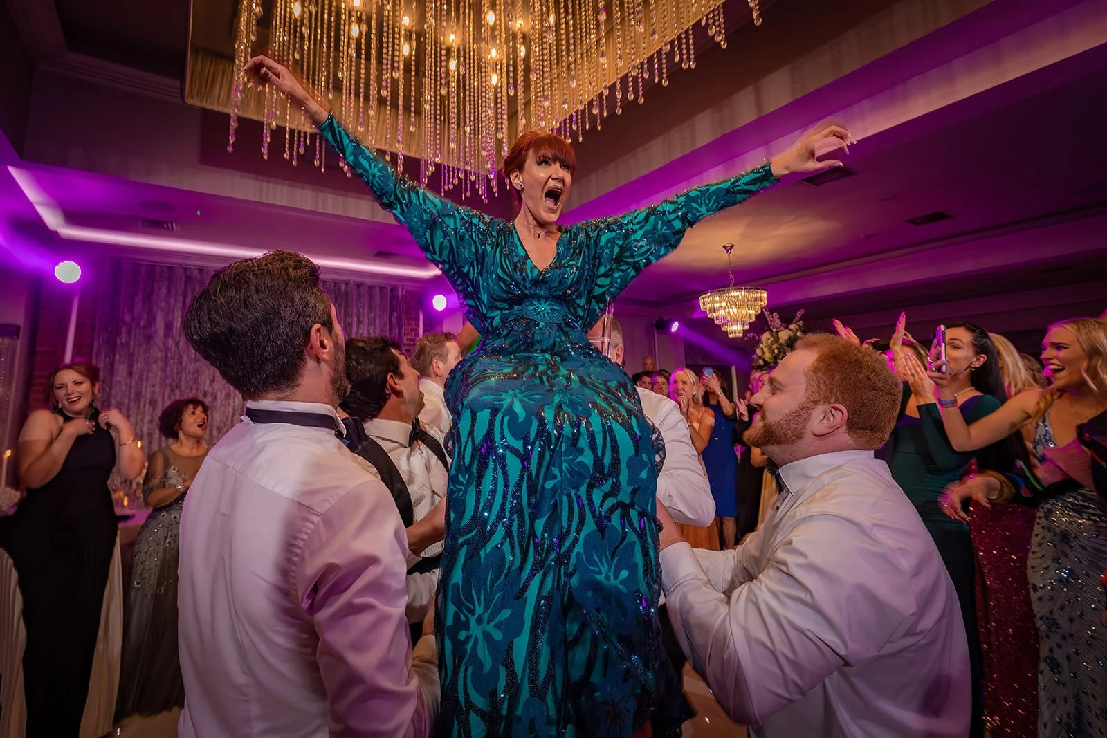 Merrydale Manor wedding guest in teal dress lifted on dance floor chandelier above – fine art wedding photographer North West