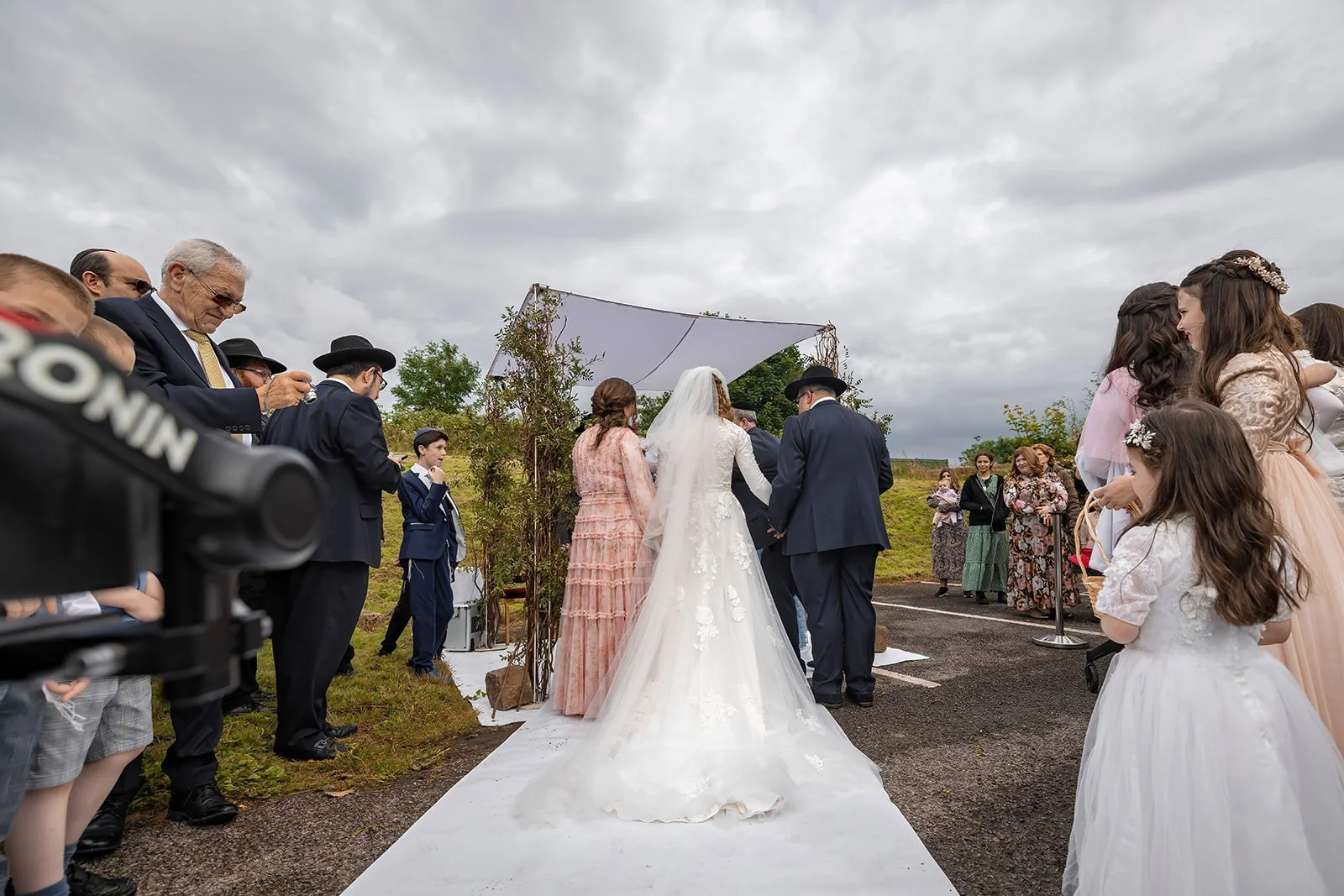 bride and parents make entrance down aisle to outdoor wedding ceremony at last drop village in bolton
