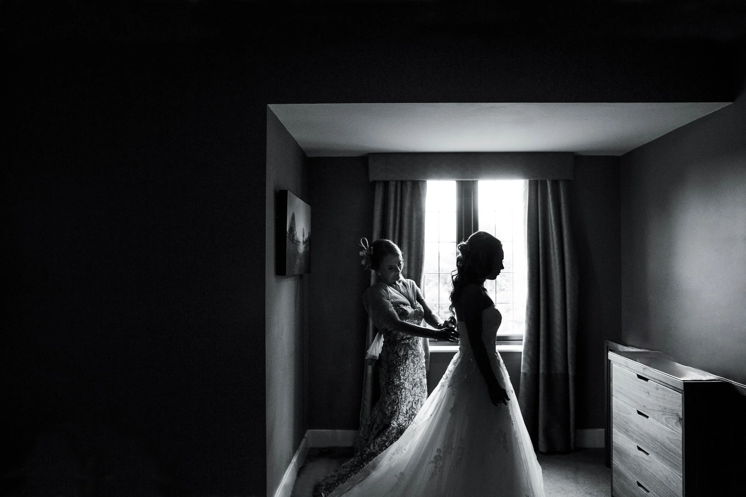 Black and white silhouette photo of bride being helped into dress during morning preparations