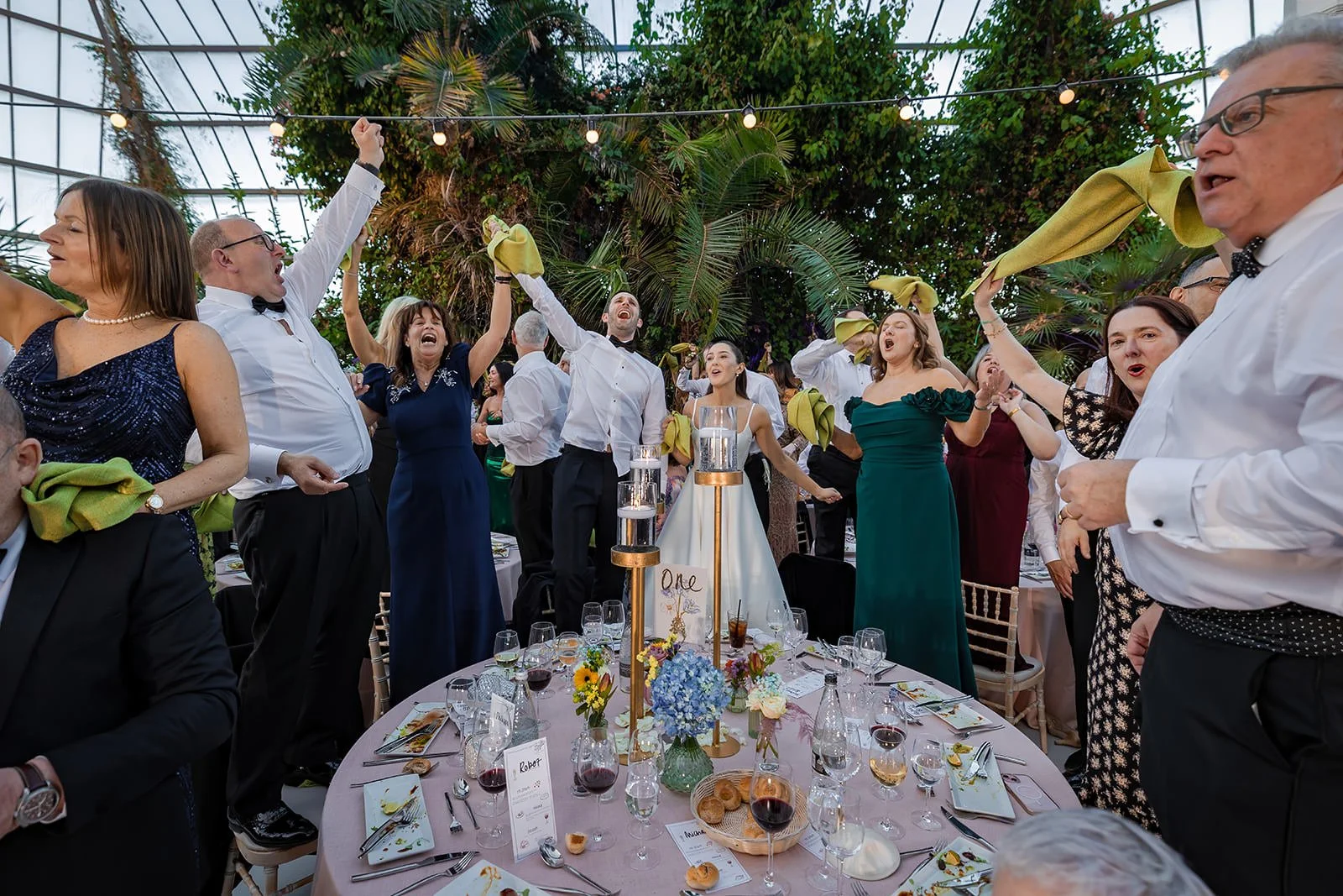 bride and groom singing on chairs at wedding reception at sefton park palm house in liverpool