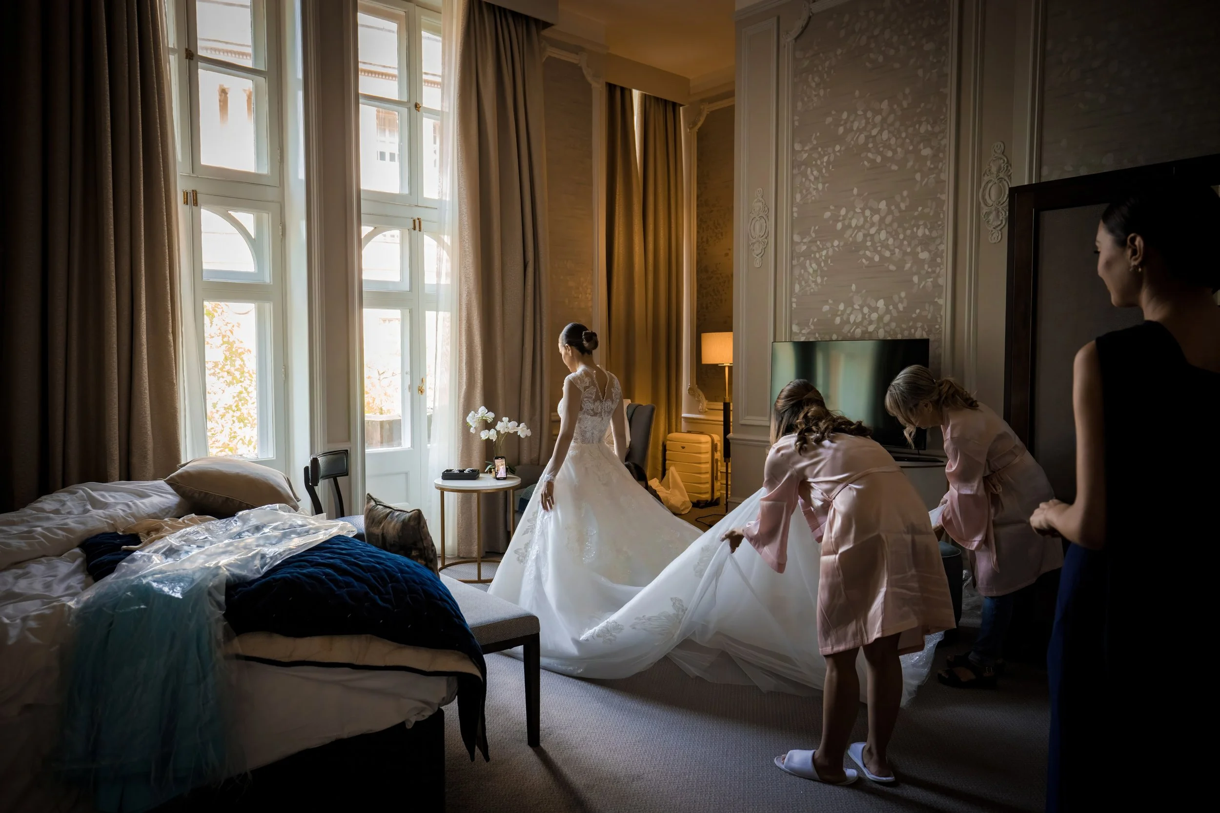 Jewish wedding photographer bride getting dress on during prep with help from bridesmaids