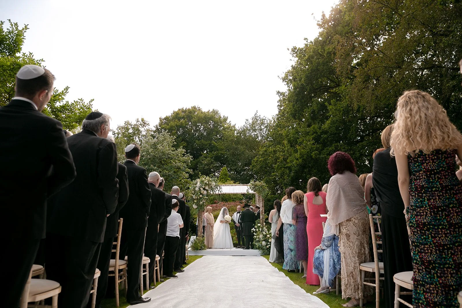 wide angle from end of aisle of bride and groom exchange vows during outdoor wedding ceremony at nunsmere hall in cheshire