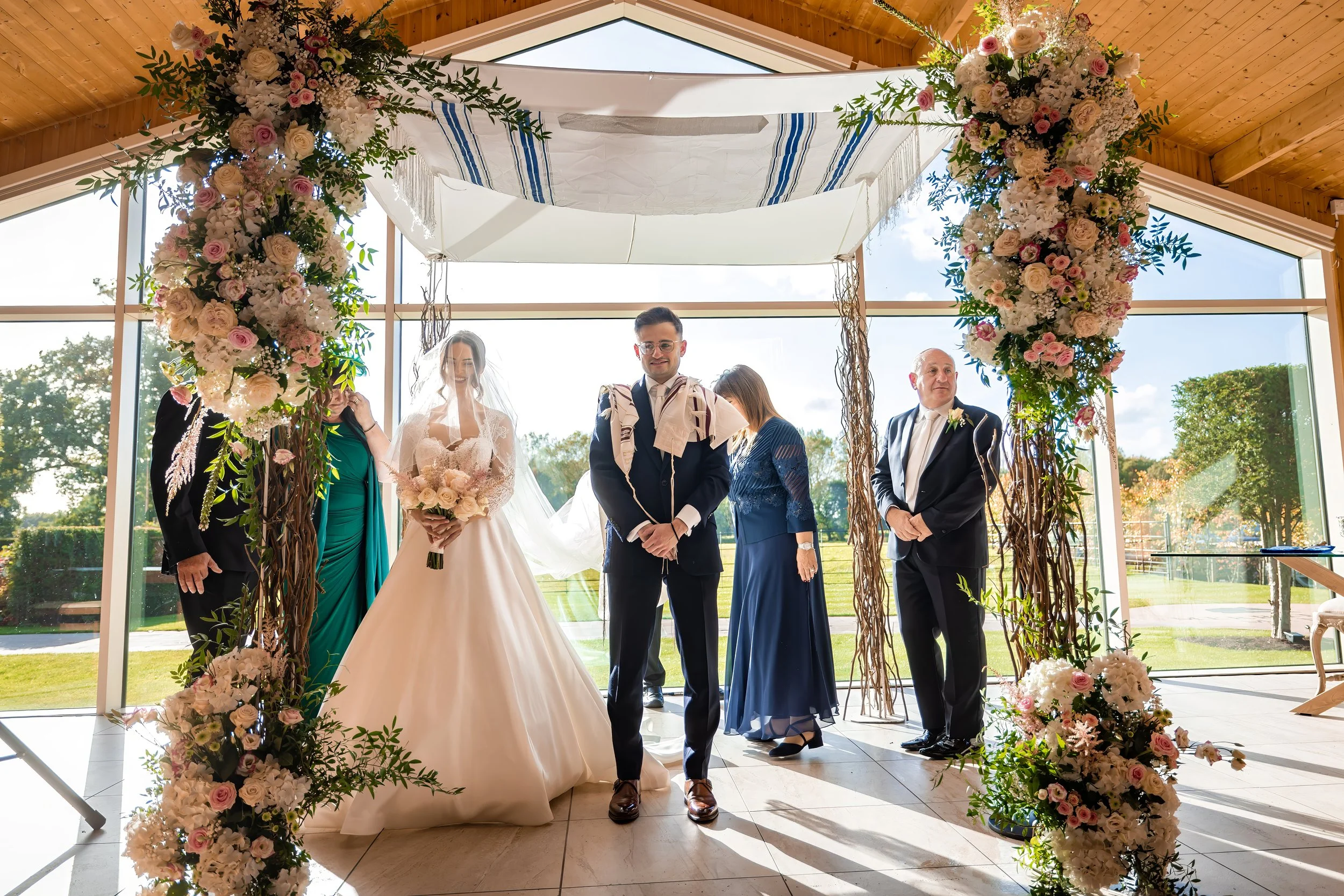 A wedding ceremony at Merrydale Manor with a bride and groom standing underneath a floral chuppah