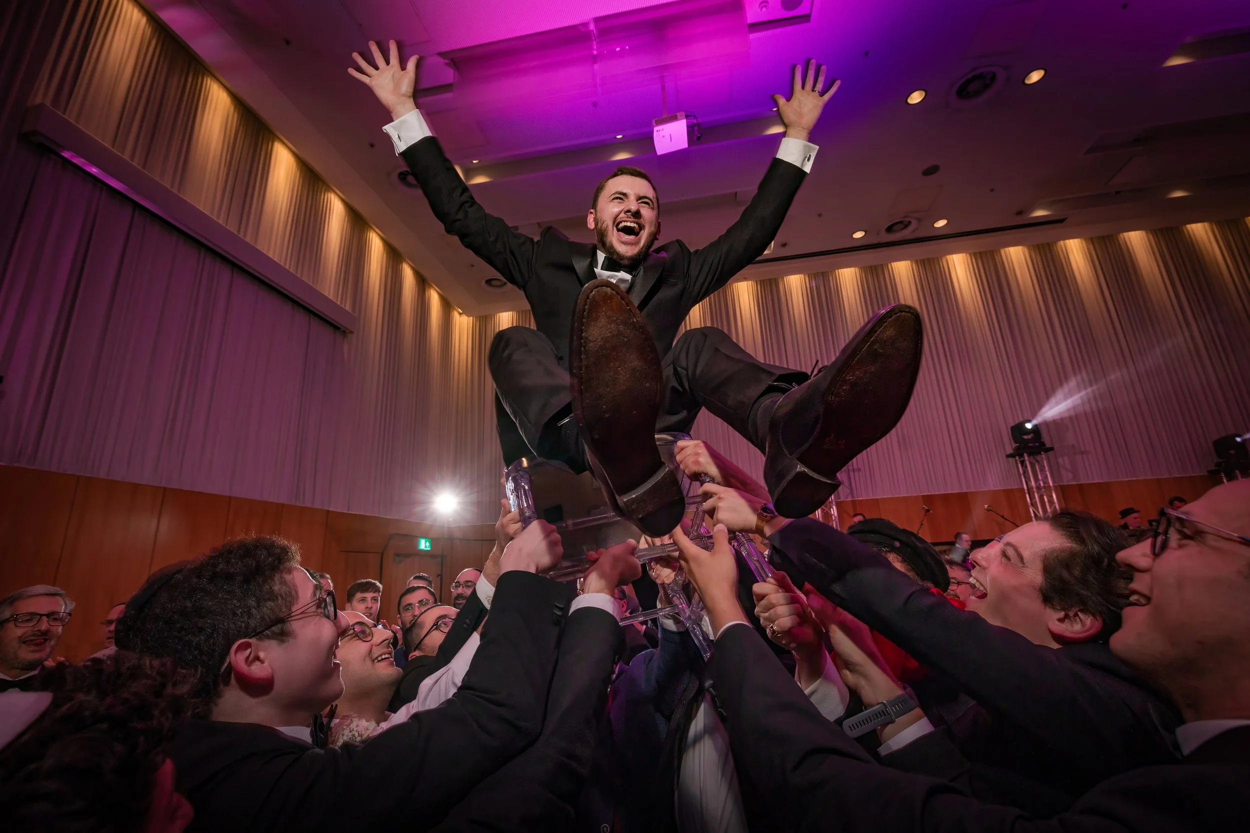 jewish groom held up on chair during hora dancing evening reception party