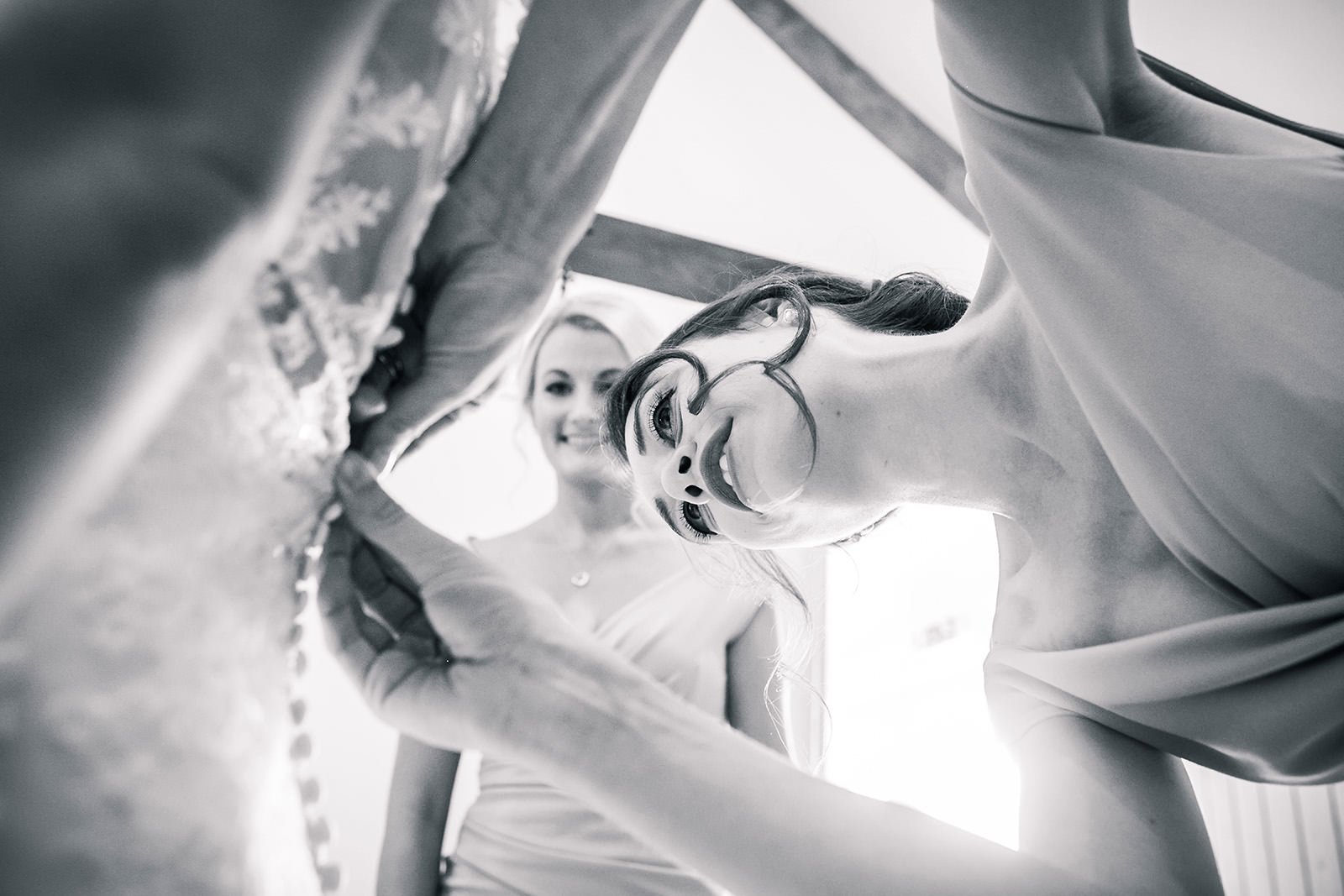 Bridesmaid adjusting buttons on bride's wedding dress during bridal prep