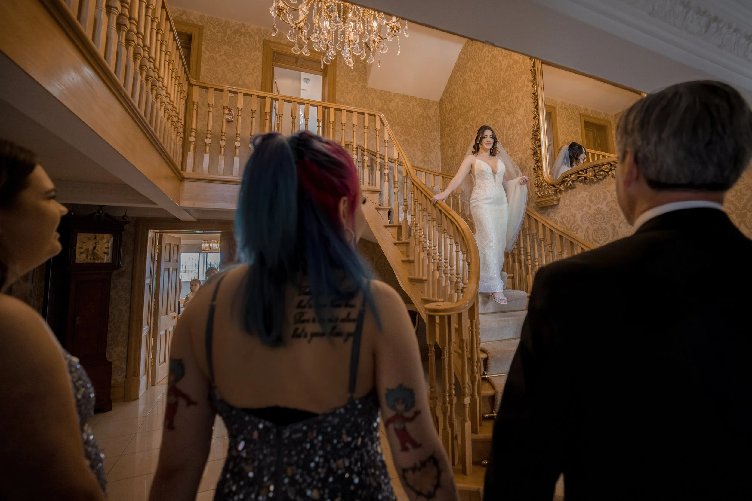 Bride walks down stairs for first look in her wedding dress with bridesmaids and dad