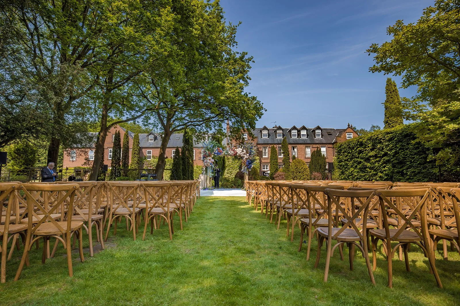 Open lawn ceremony setup with arch and wooden chairs, Nunsmere Hall Cheshire