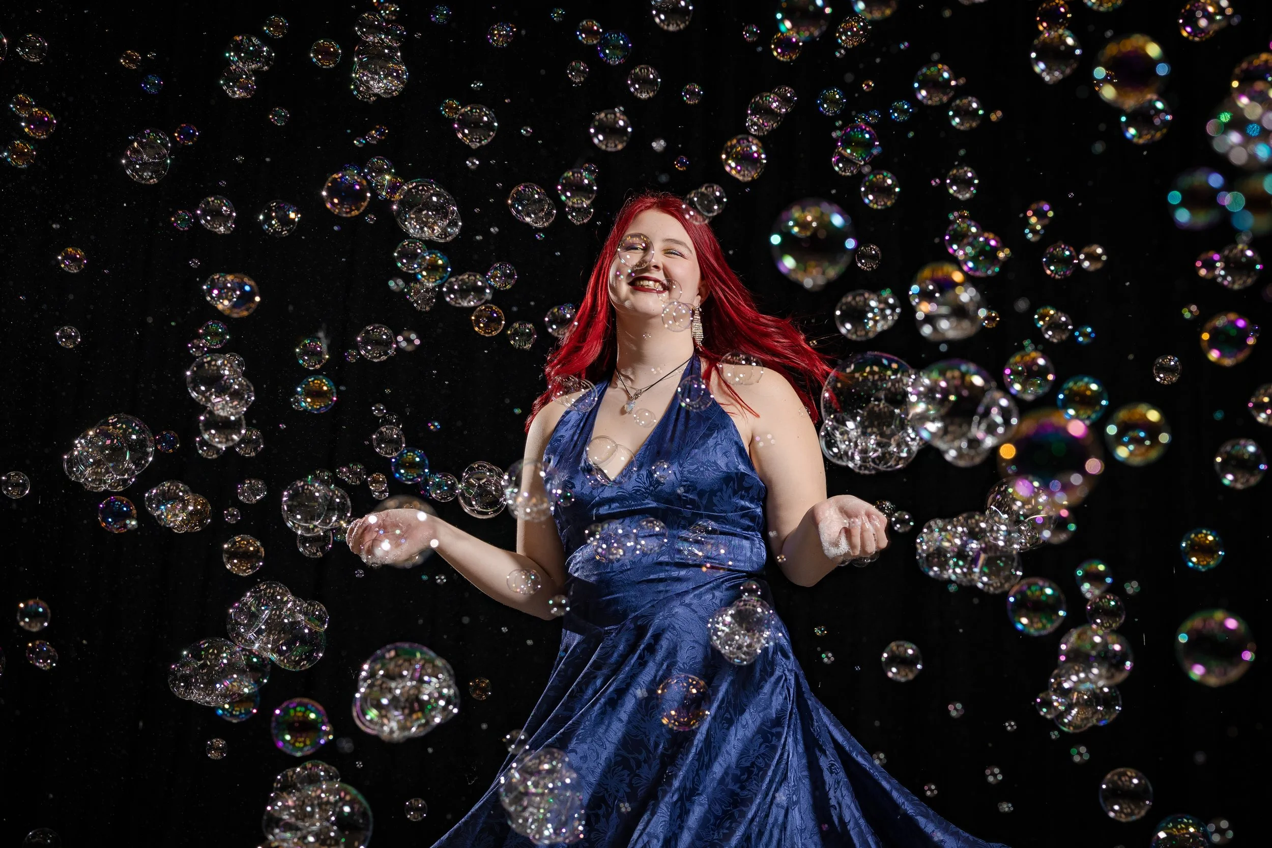 PR Photographer Manchester — female bubble performer in blue velvet gown laughing joyfully surrounded by hundreds of iridescent bubbles, Manchester Bubble Festival