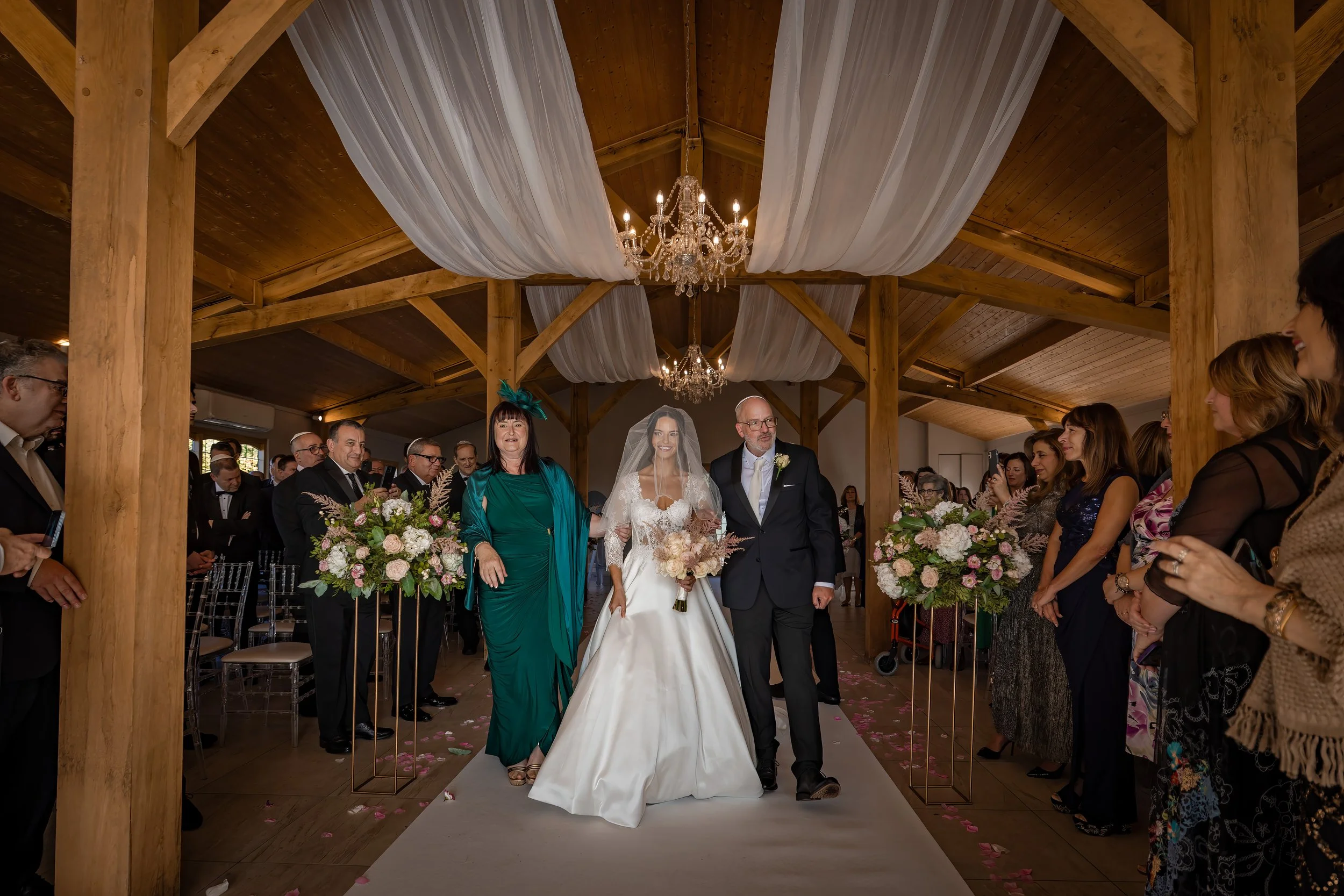 bride walks down aisle with parents during wedding ceremony at merrydale manor in cheshire