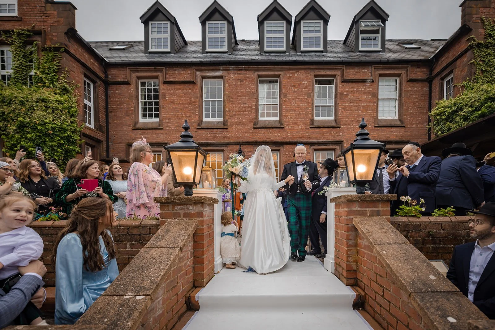 Bride walking through lantern-flanked main entrance of Nunsmere Hall in evening light
