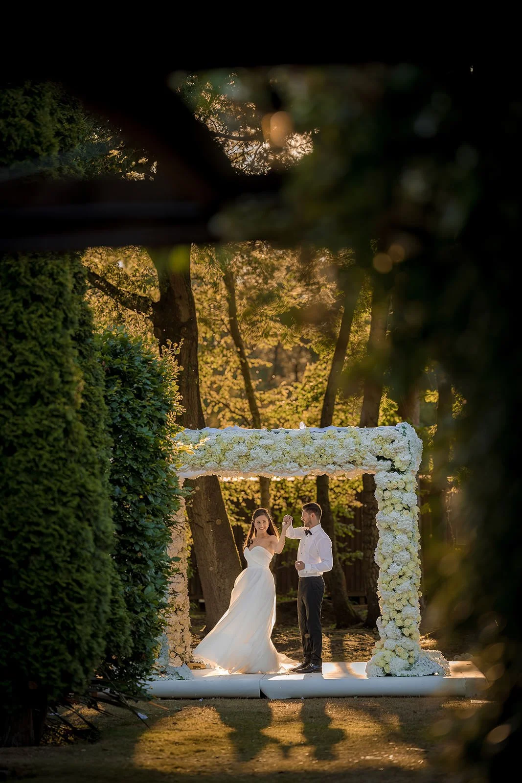 Couple at floral arch framed through golden autumn foliage, Nunsmere Hall grounds
