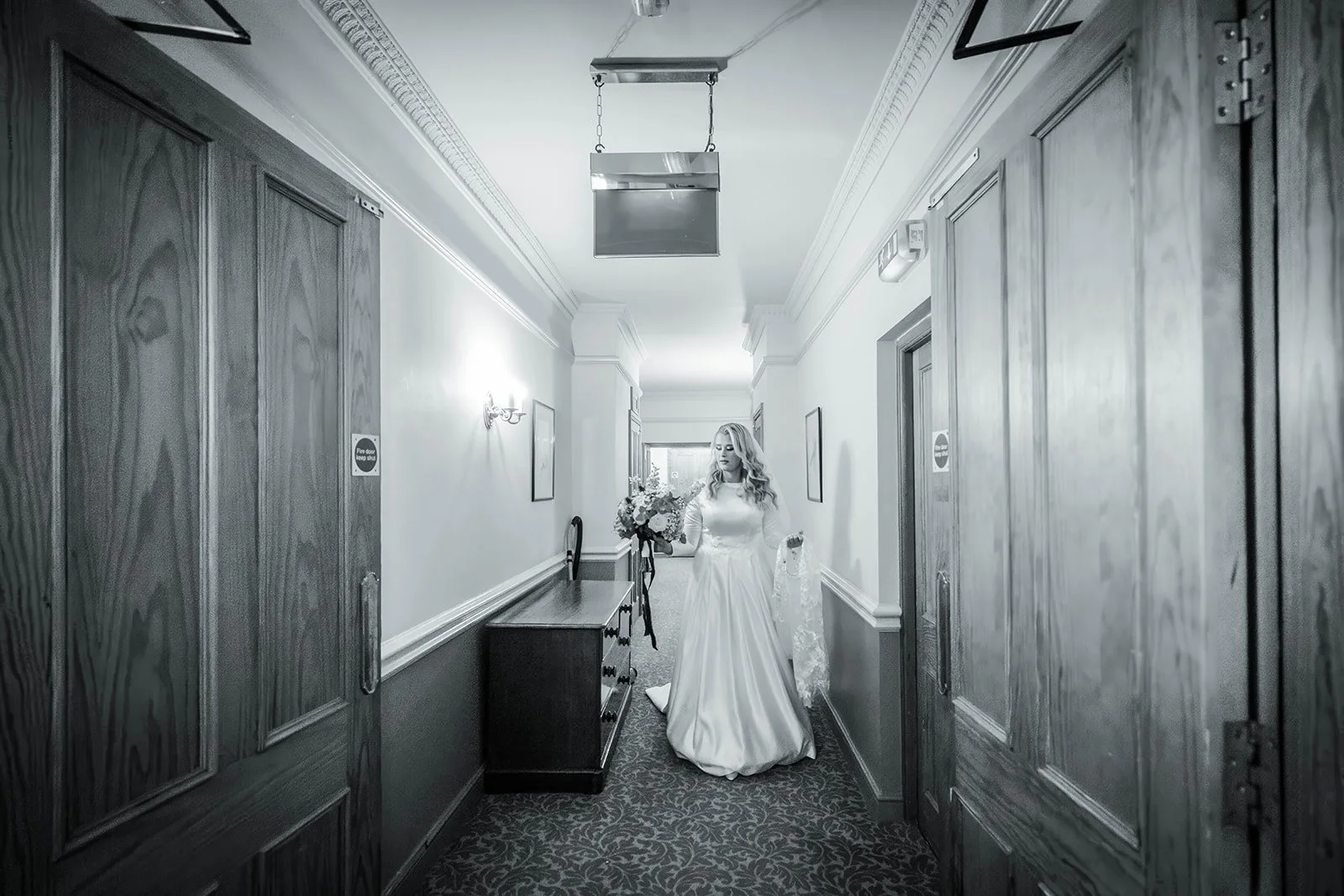 Black and white - bride walking down elegant corridor at Nunsmere Hall before the ceremony