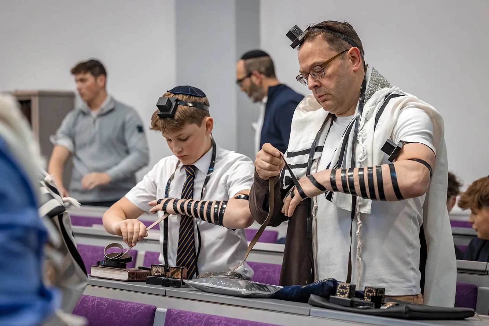 barmitzvah boy and dad wrapping their tefillin together during service in synagogue