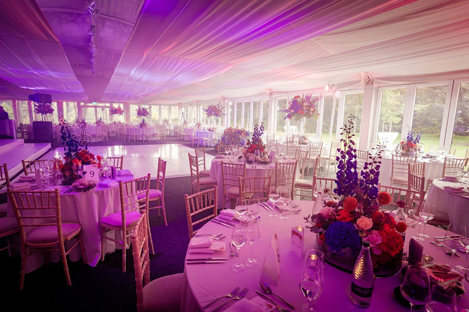 Nunsmere Hall marquee wedding breakfast setup with floral centrepieces, pink lighting
