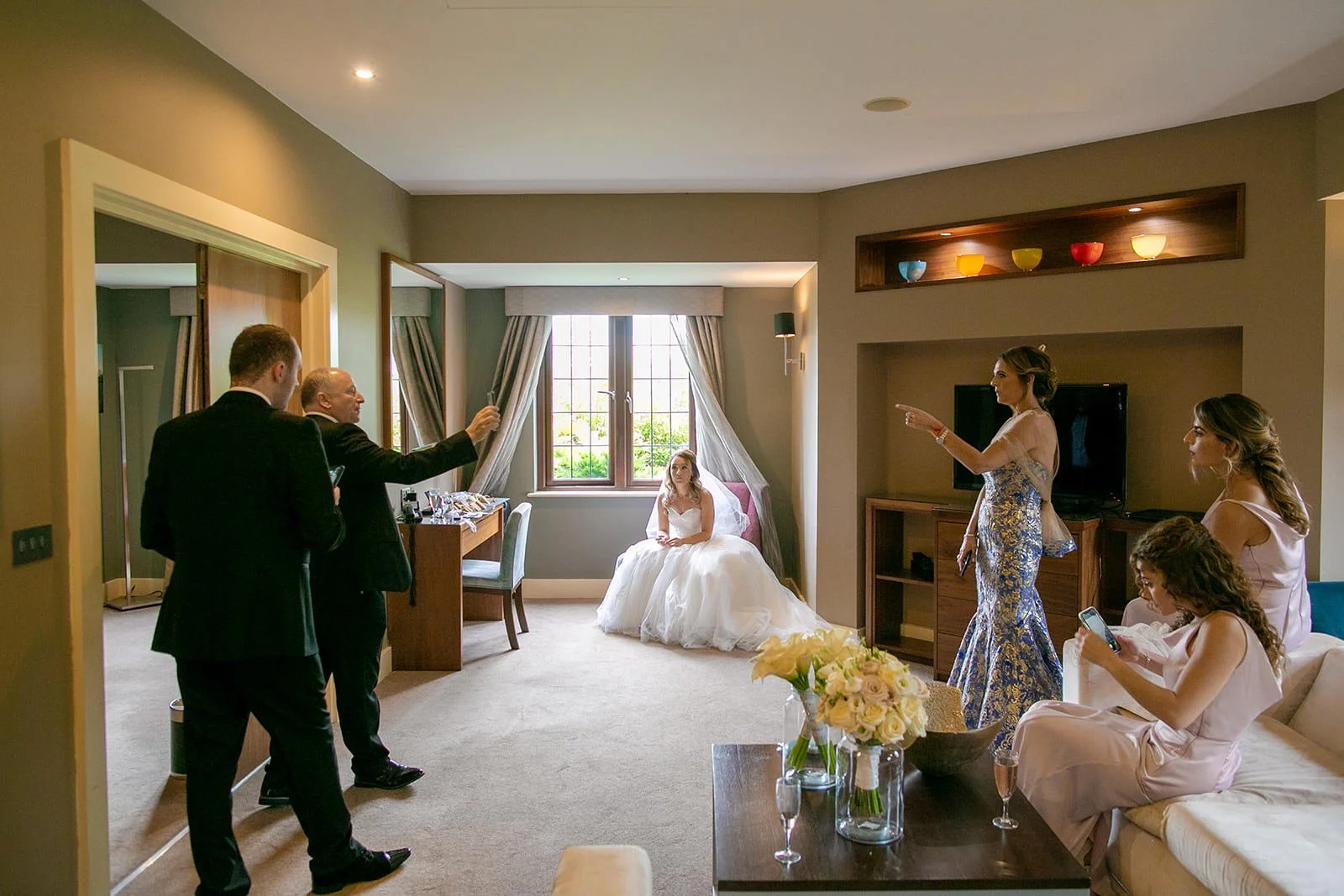 Wide bridal prep suite at Fairmont Cheshire - The Mere, bride in wedding dress by window
