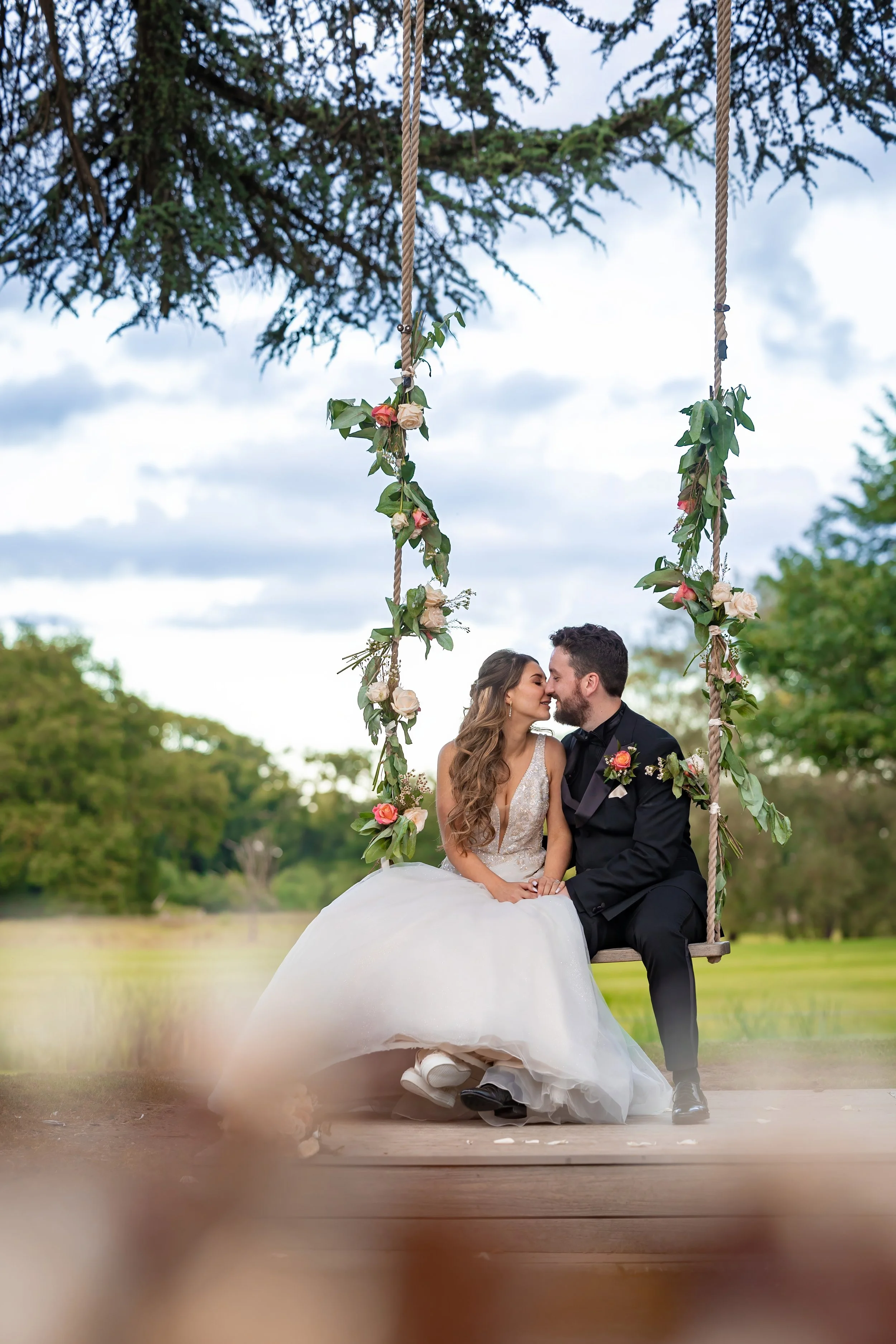 Jewish wedding photographer in manchester captures Jewish bride and groom newlywed couple portraits kissing on floral decorated swing