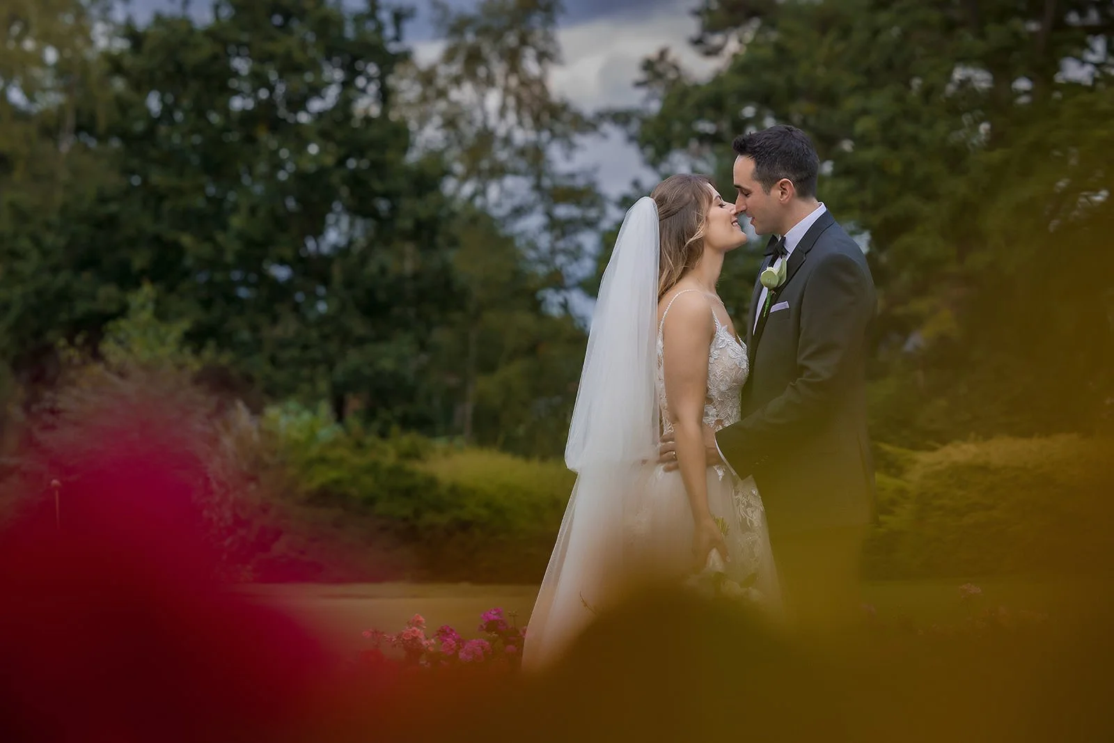 Couple portrait framed through soft foliage, garden grounds at The Mere Knutsford
