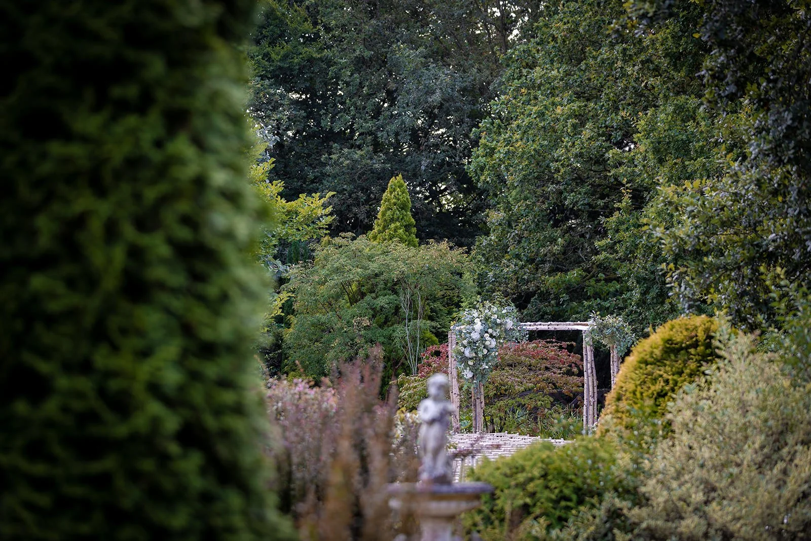 chuppah visible through foliage at outdoor ceremony in Italian gardens, Nunsmere Hall
