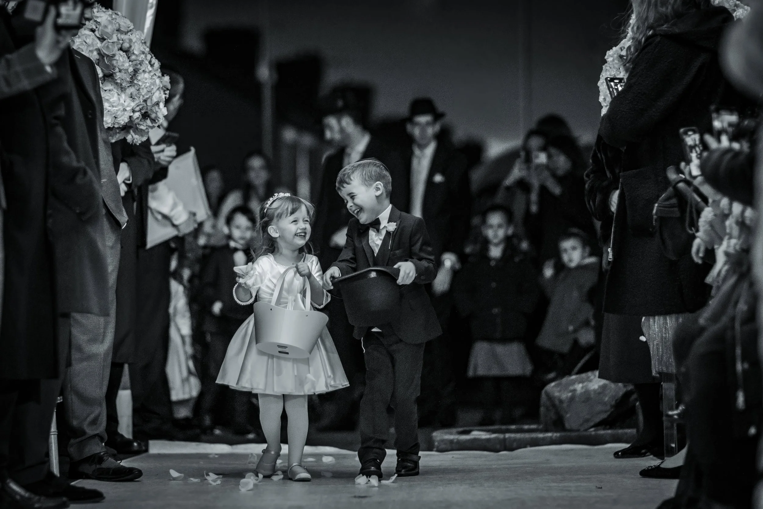 cute page boy and flower girl walk down aisle at charedi jewish wedding ceremony