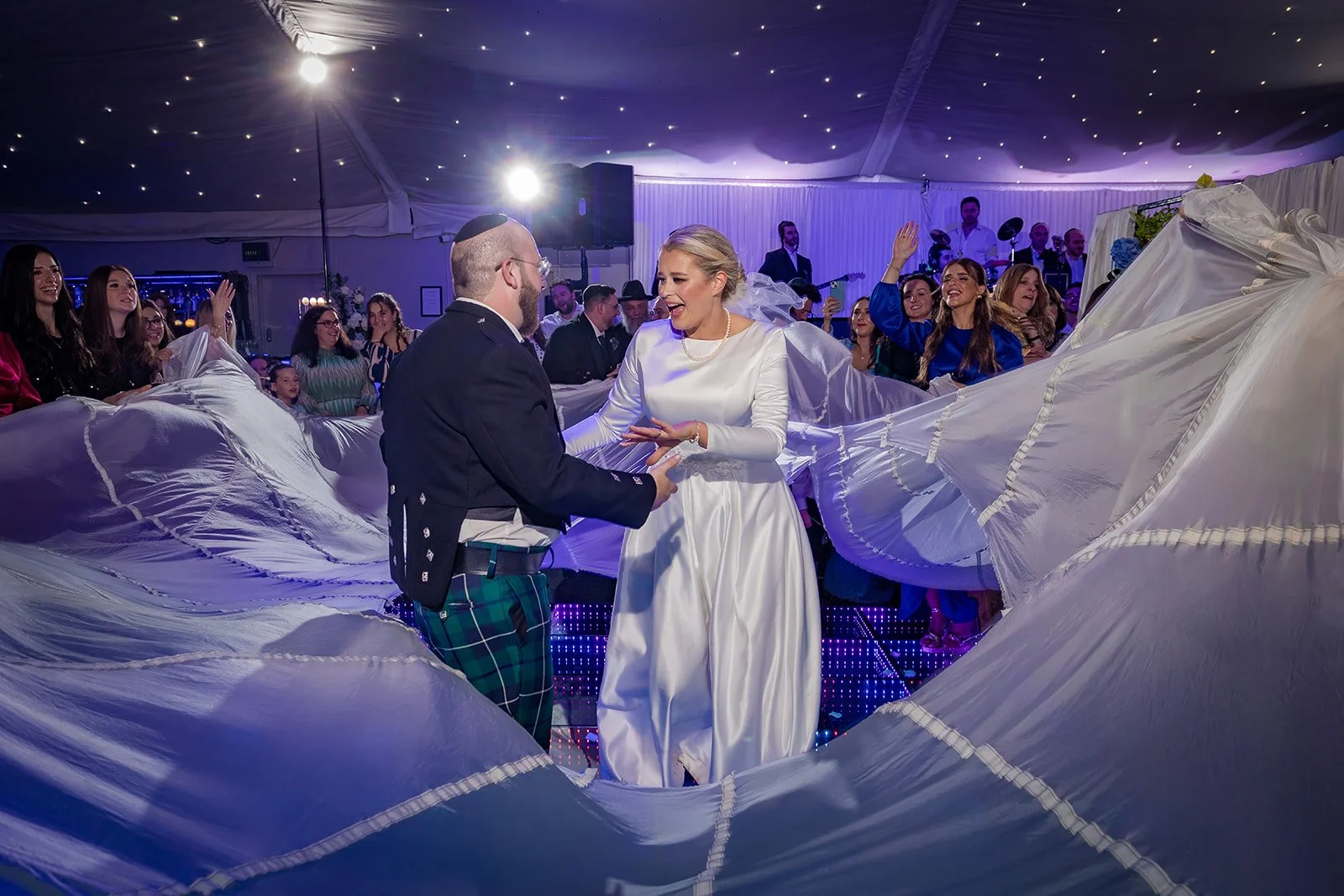 Bride and groom in sheet during energetic dancing in Nunsmere Hall wedding marquee
