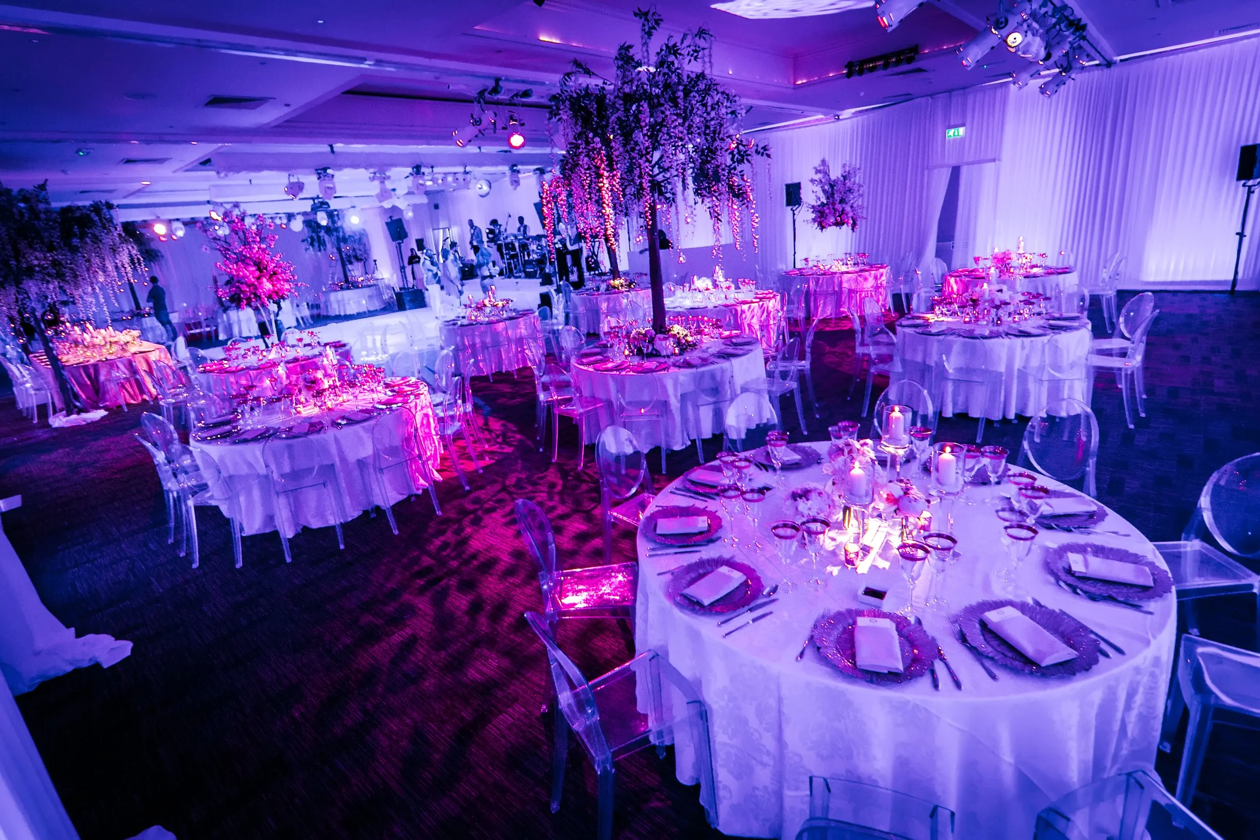 Round tables with tall floral centrepieces under pink lighting, The Mere wedding breakfast
