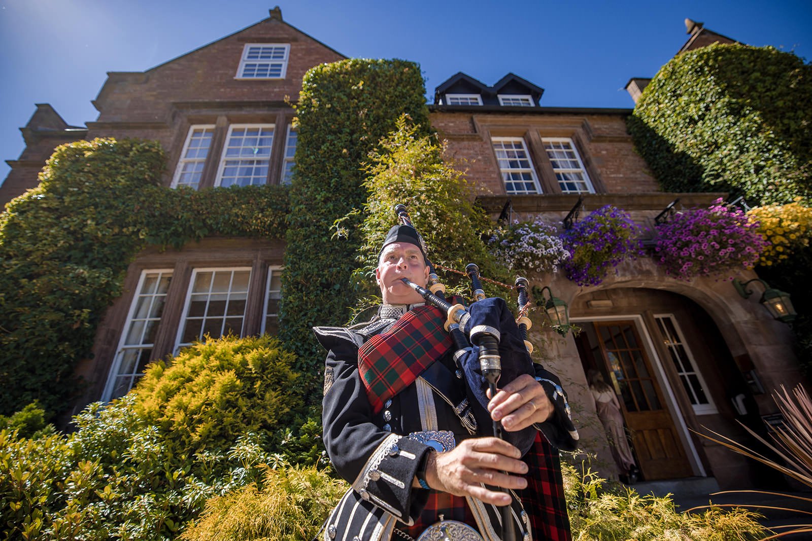 Bagpiper in tartan kilt performing outside Nunsmere Hall at a wedding
