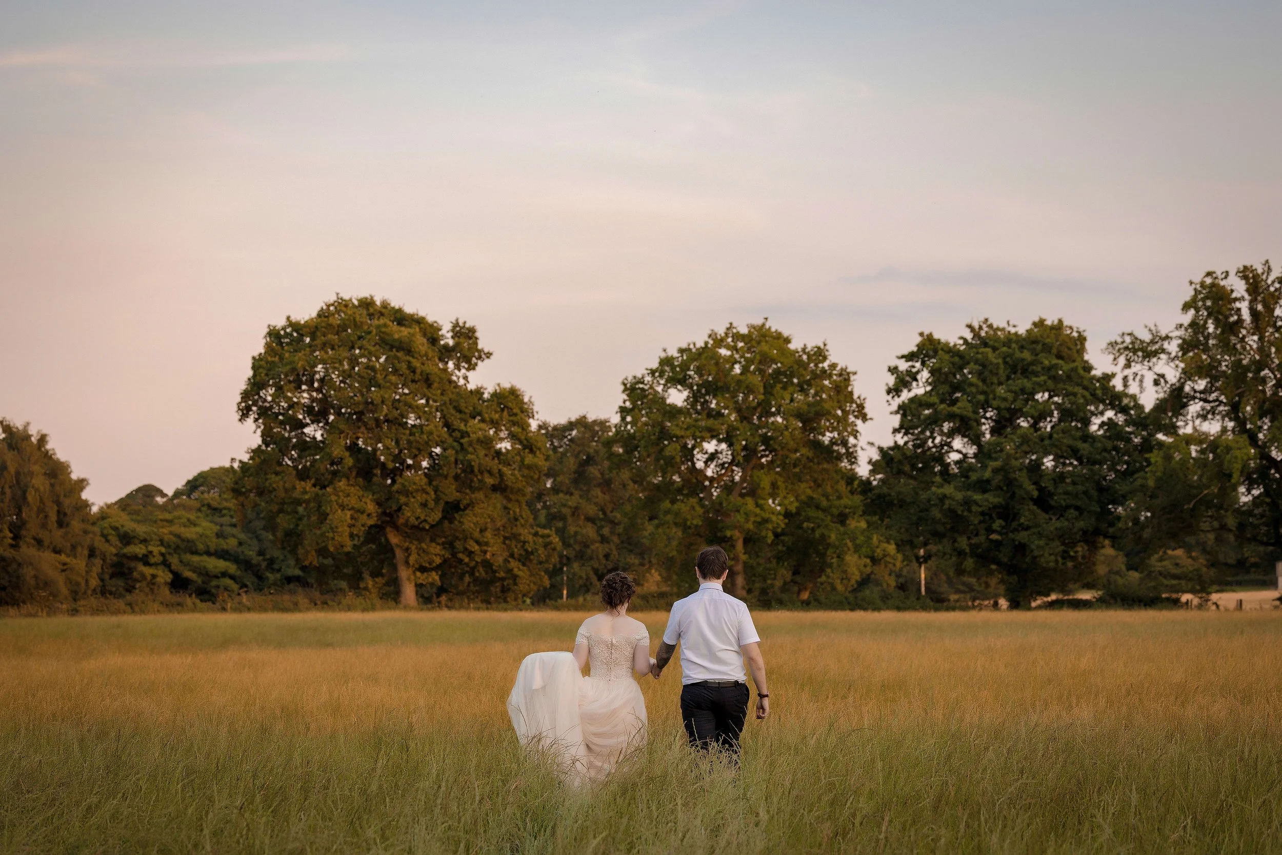 Manchester wedding photographer portrait of bride and groom walking away in a field