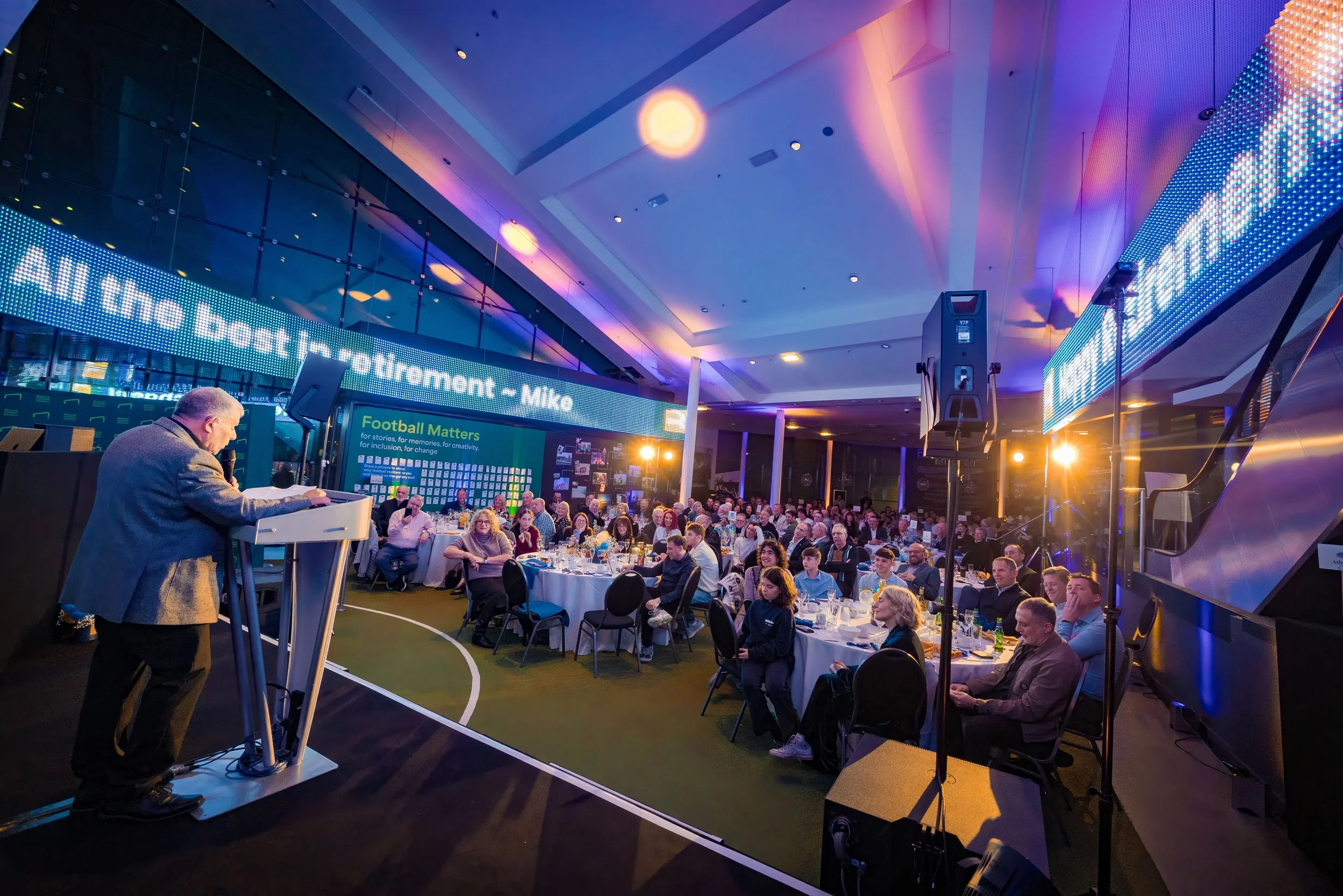 Business Event Photographer Manchester — speaker at a lectern on stage at a corporate retirement dinner