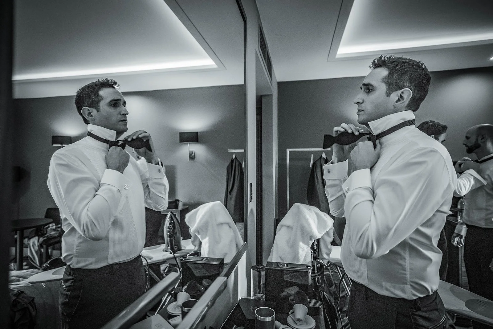 Black and white - groom adjusting tie in hotel room mirror, The Mere Knutsford
