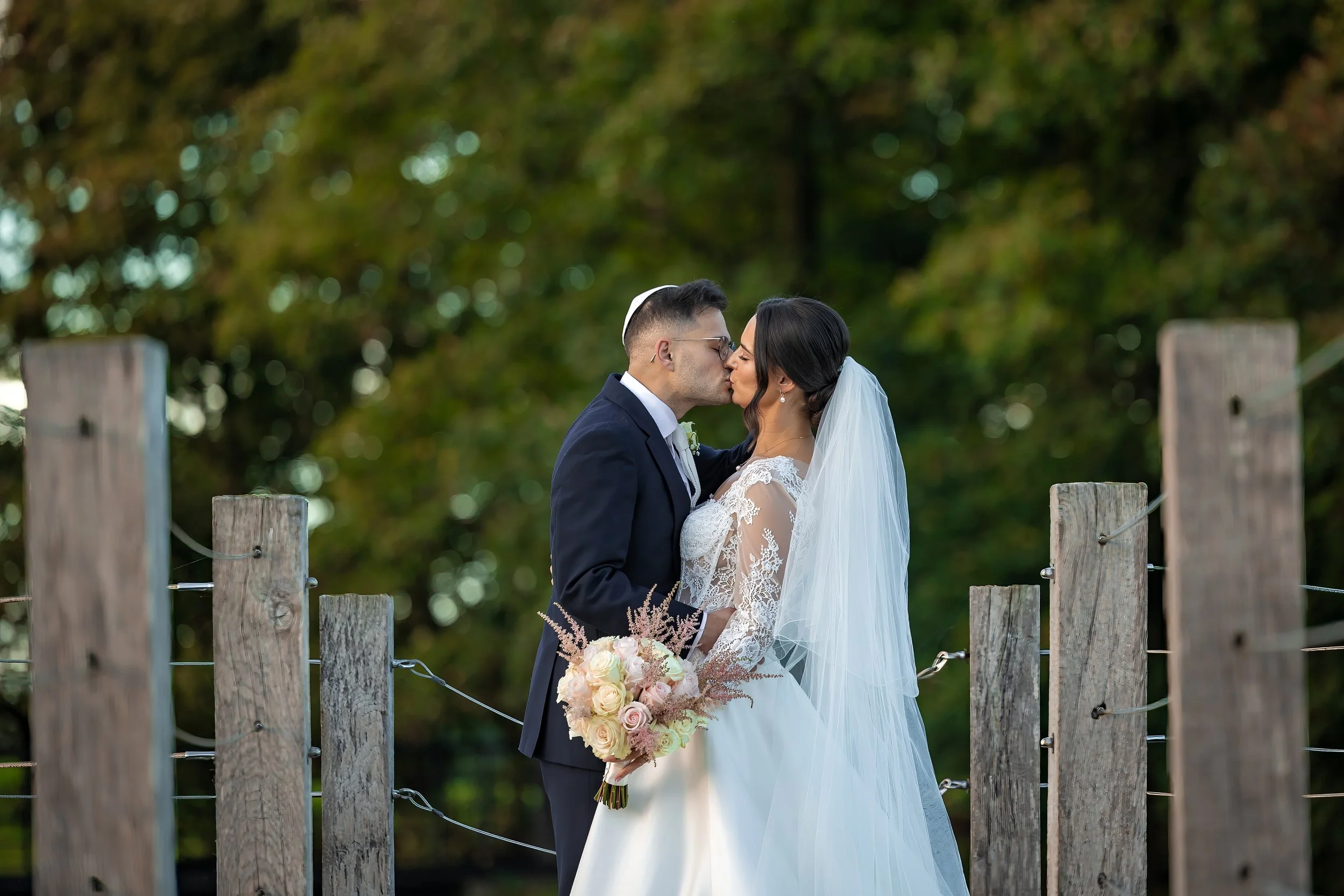 Merrydale Manor wedding couple kissing by wooden fence outdoors – documentary wedding photographer Manchester