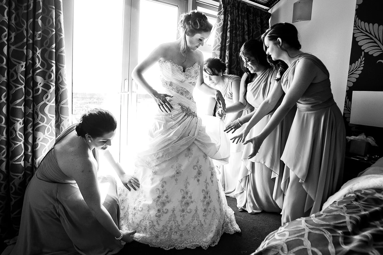 Bridesmaids offer helping hand with bride's wedding dress during bridal prep