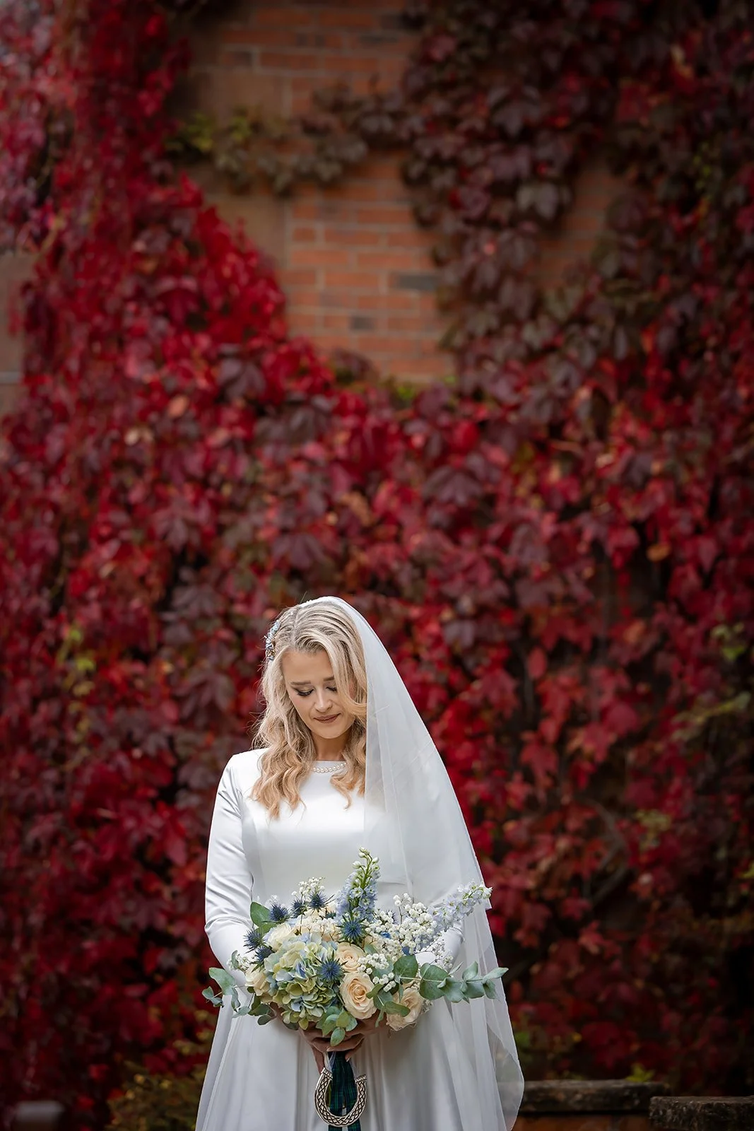 Bride with bouquet against red autumn ivy on Nunsmere Hall red brick wall