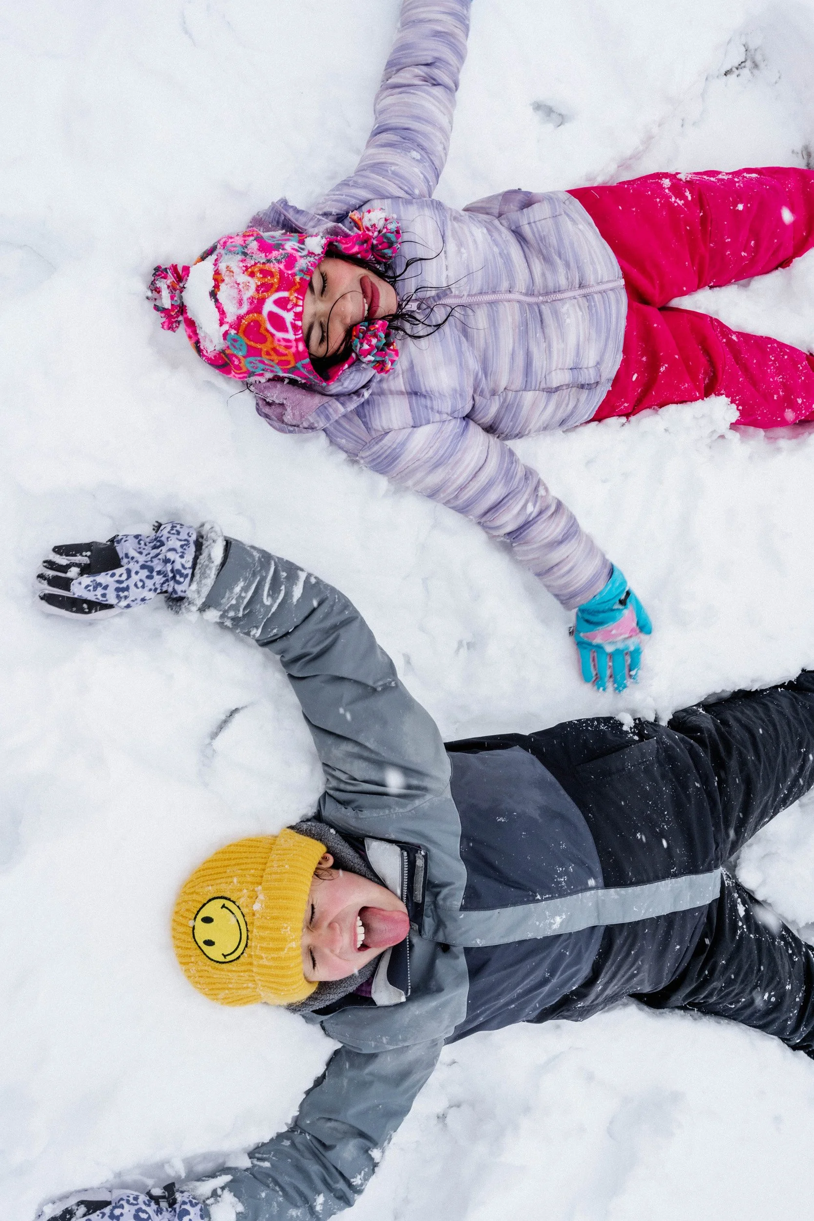 A group of children lying in the snow making snow angels, dressed warmly with colorful winter clothing and hats.